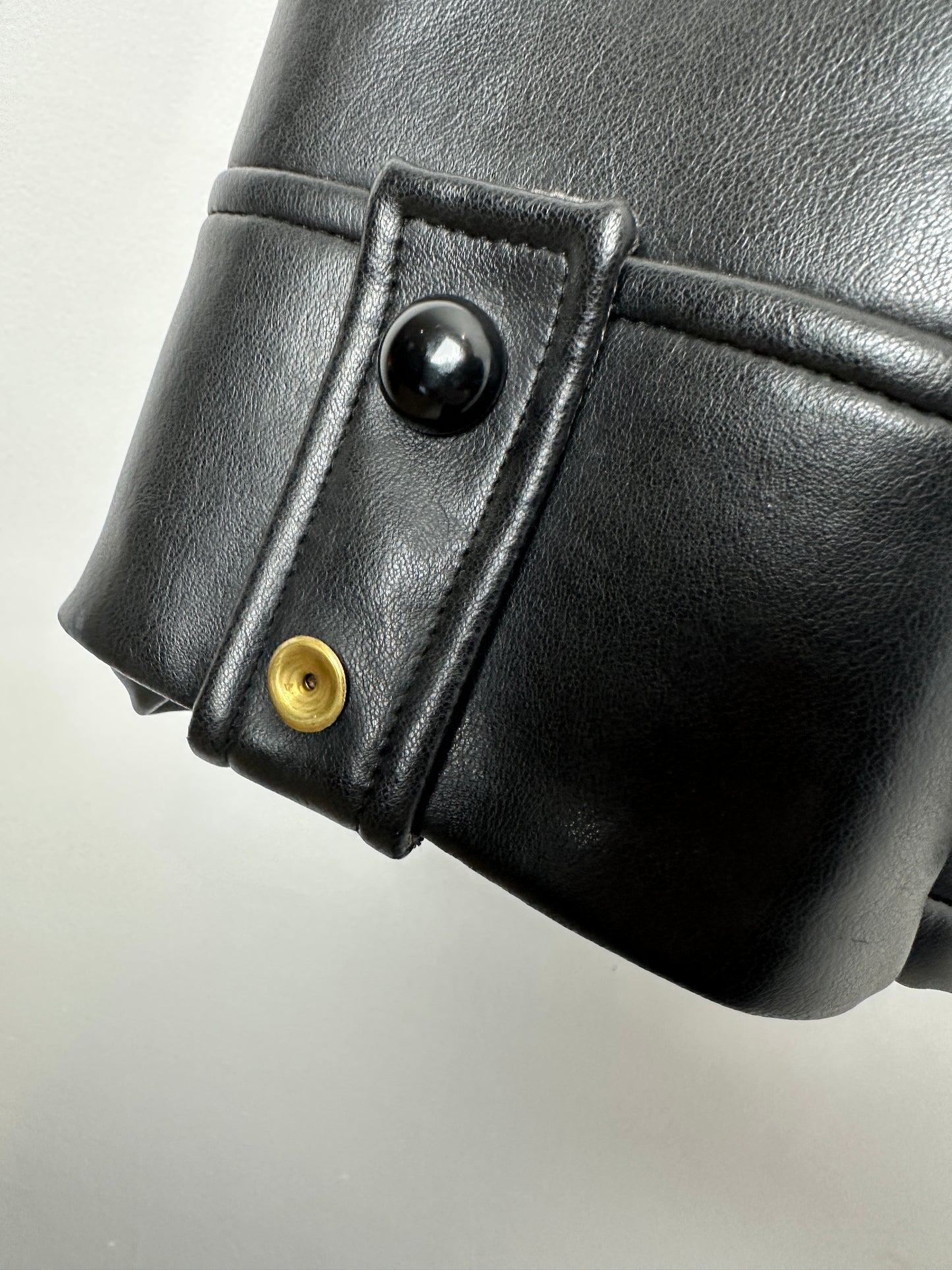 Close-up of a black leather sleeve with a button and gold accent on a light gray background
