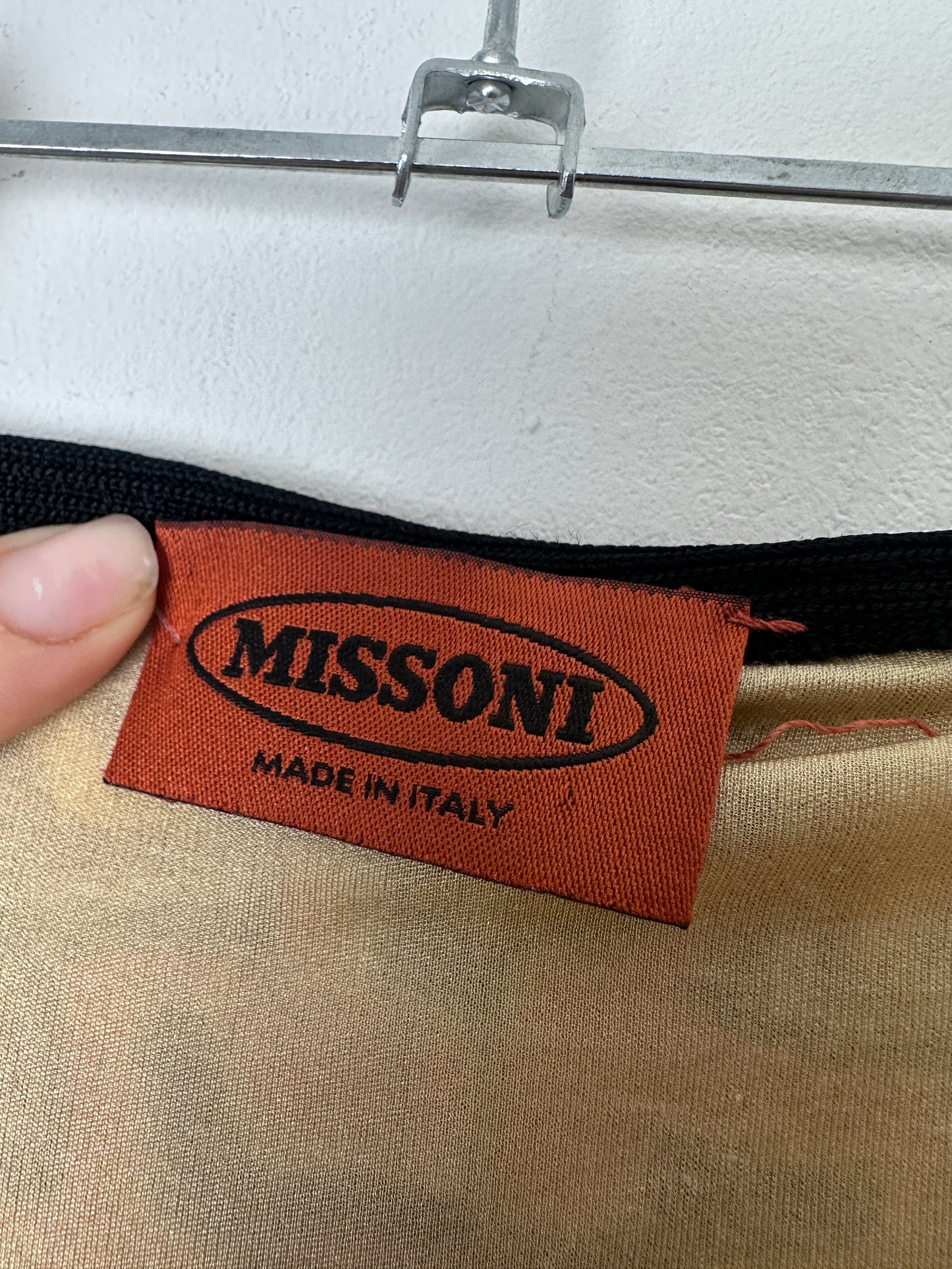 Close-up of a brown Missoni fabric label with black text reading 'Missoni Made in Italy' attached to a garment, with a finger holding it in place.