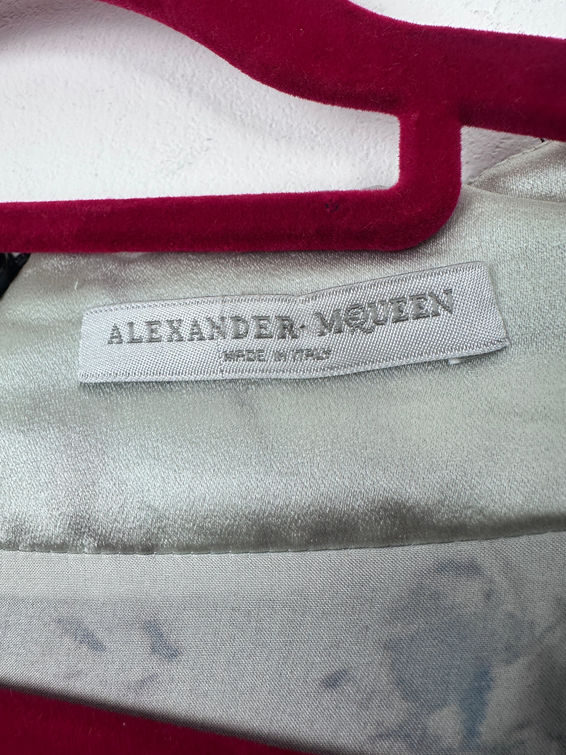 Close-up of a garment label reading ALEXANDER MOUZEN MADE IN ITALY, showing part of a white and deep red garment with a shiny silver-gray satin-like fabric.