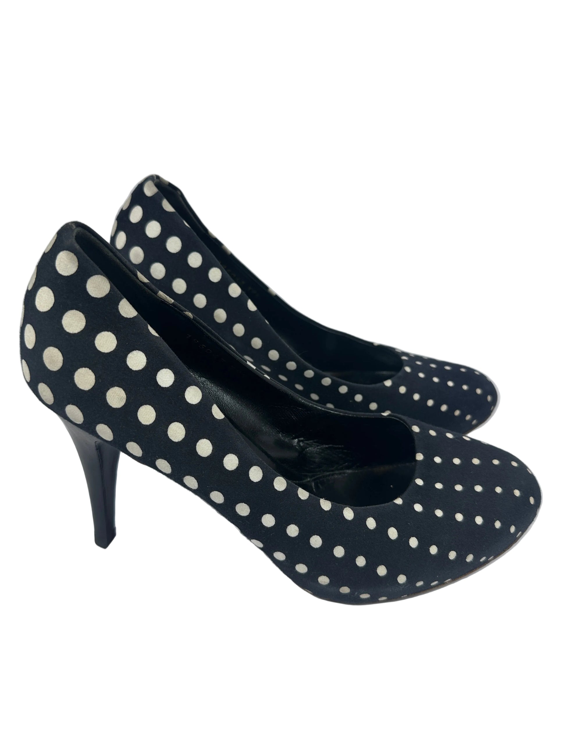 A pair of black pointed-toe high heels with a white polka dot pattern, photographed on a plain light gray background.
