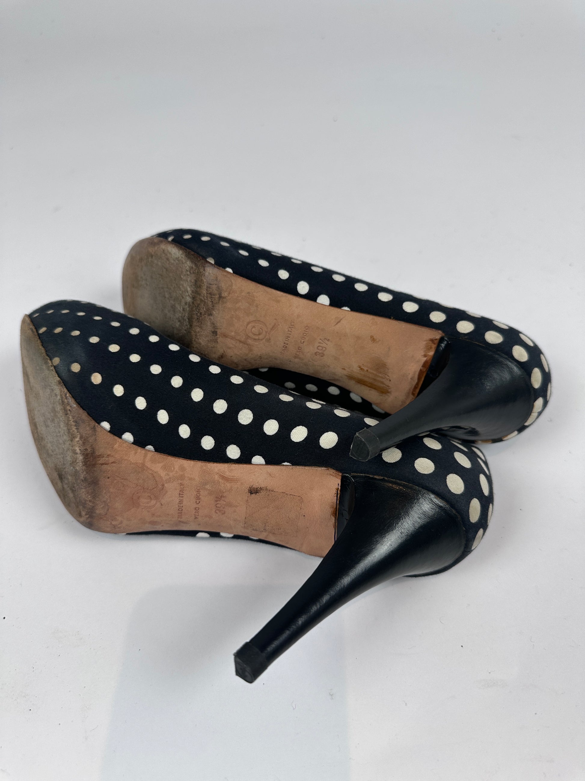 A pair of women's high-heeled pumps with a black base covered in white polka dots, shown from the sole side against a plain white background.