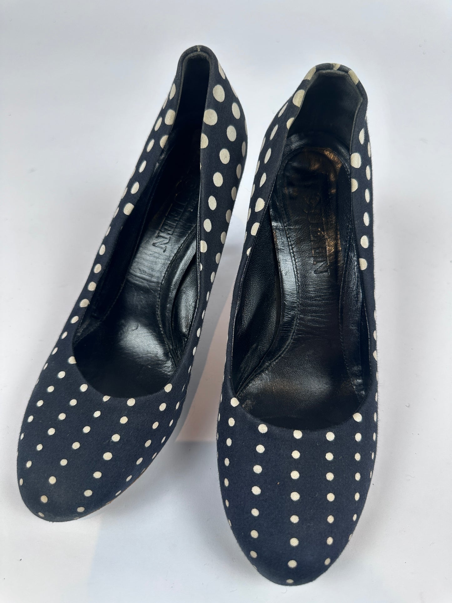 A pair of black leather slip-on heels with white polka dots, shown from a top-down view on a white background.