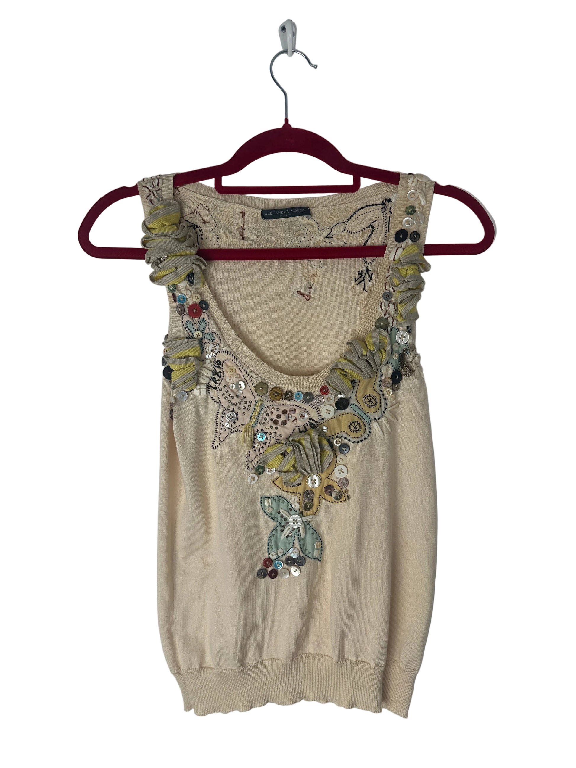 Beige top with floral embroidery on a hanger against a white background