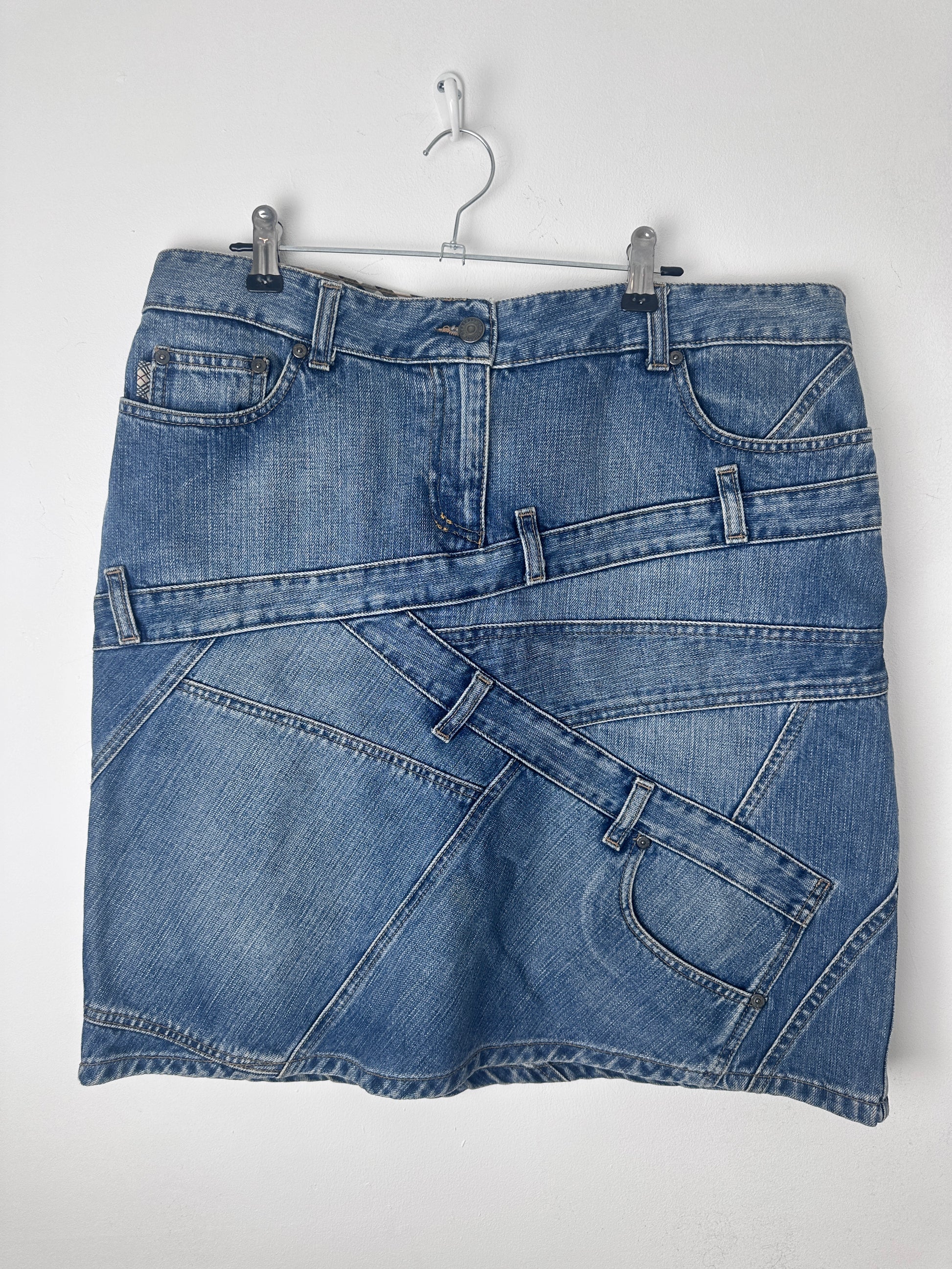 A blue denim skirt with a patchwork design of different denim panels, shown hanging on a metal hanger against a plain white background.