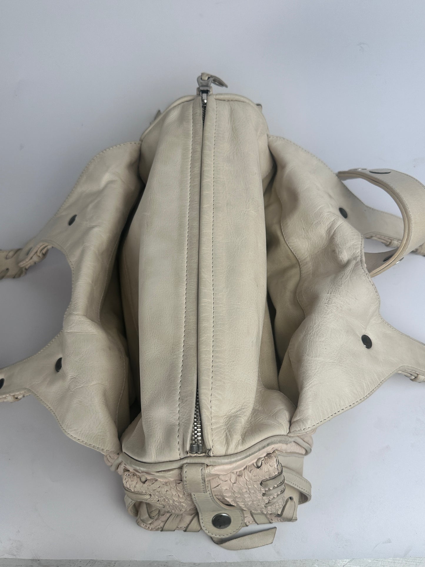 A distressed off-white leather shoulder bag with a prominent horizontal zippered compartment and a textured snakeskin-patterned side pocket, shown on a plain light background.