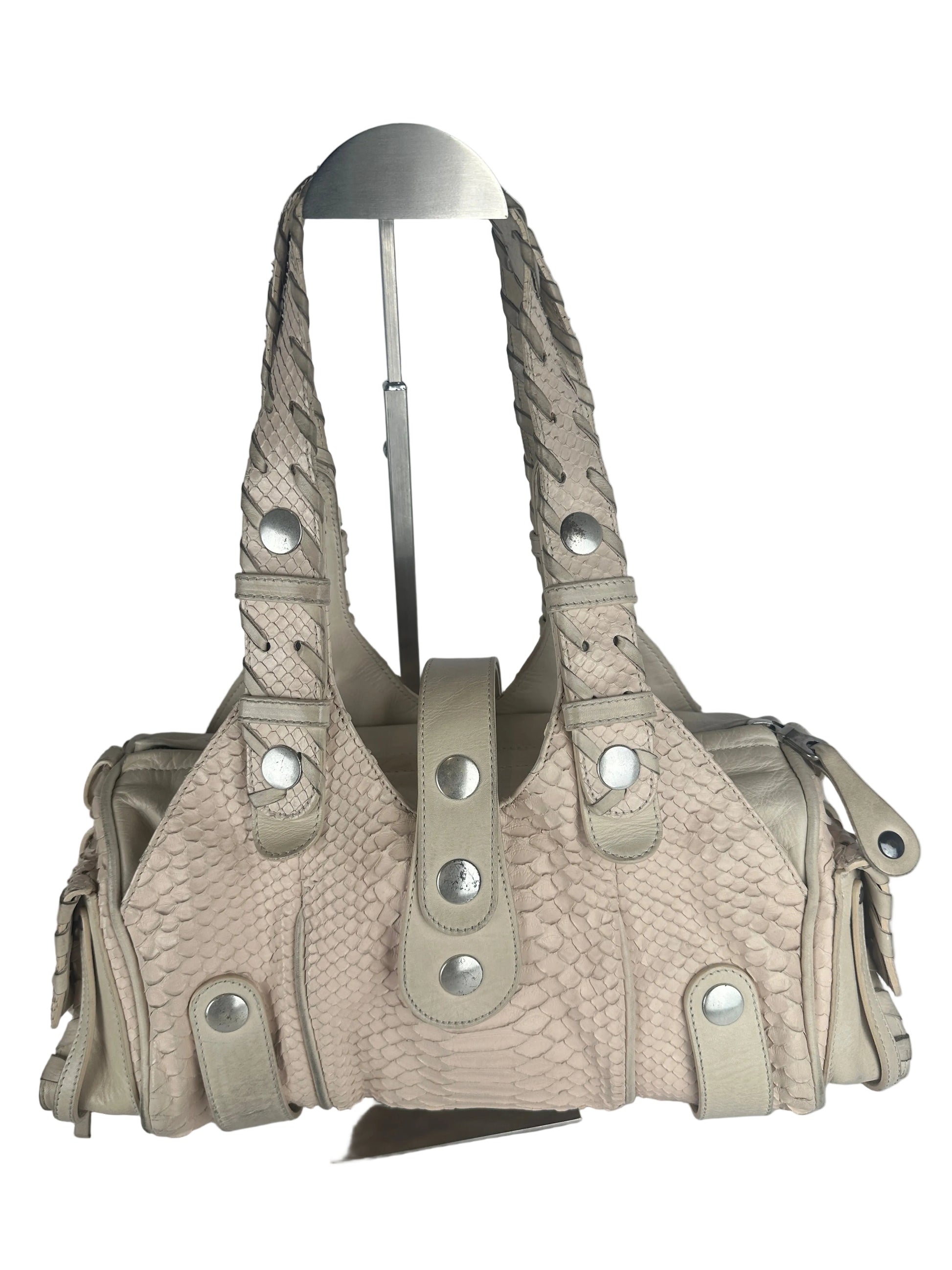 A light beige textured handbag with a braided shoulder strap and silver-tone metal studs, displayed on a metal hanger against a plain gray background.