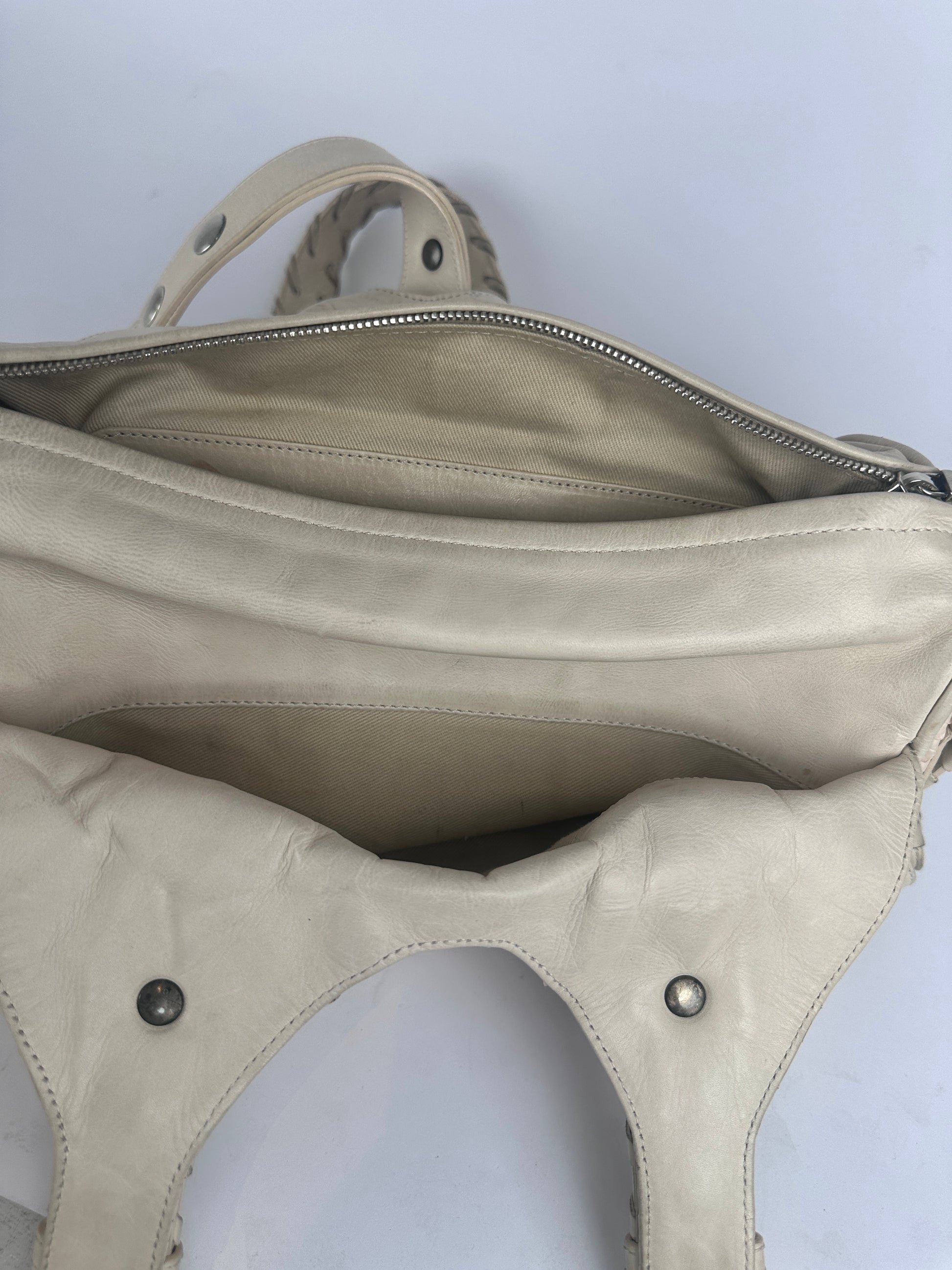 Close-up of a light beige leather shoulder bag showing the interior lining, zipper, and strap attachment details against a plain light background.