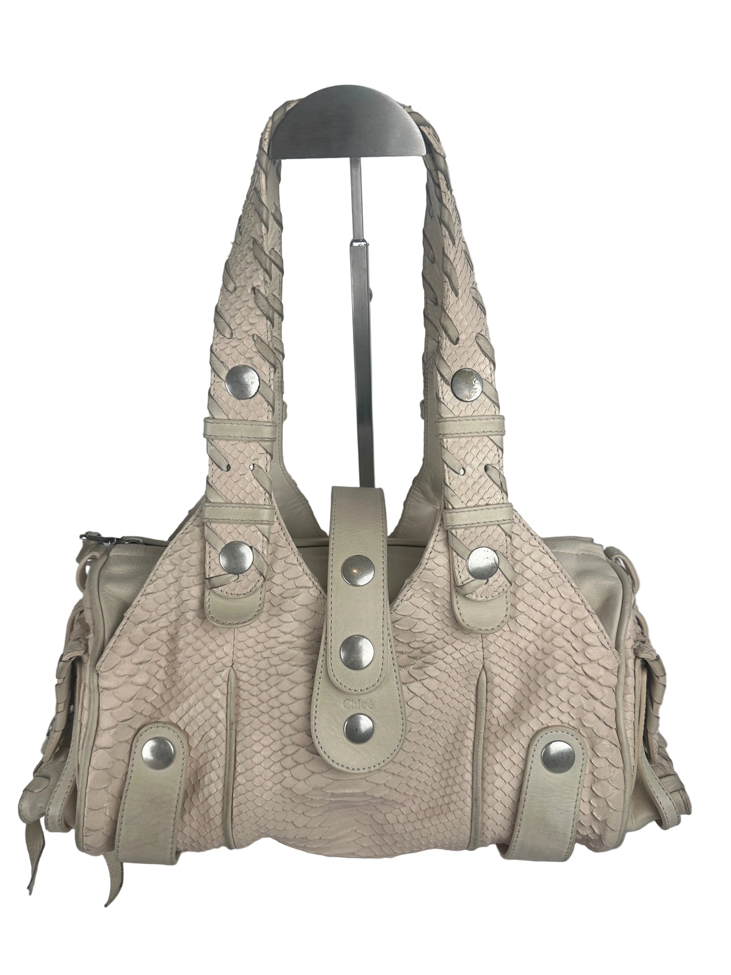 A light beige textured leather shoulder bag with braided strap details and silver-tone snap buttons, shown on a plain light gray background.