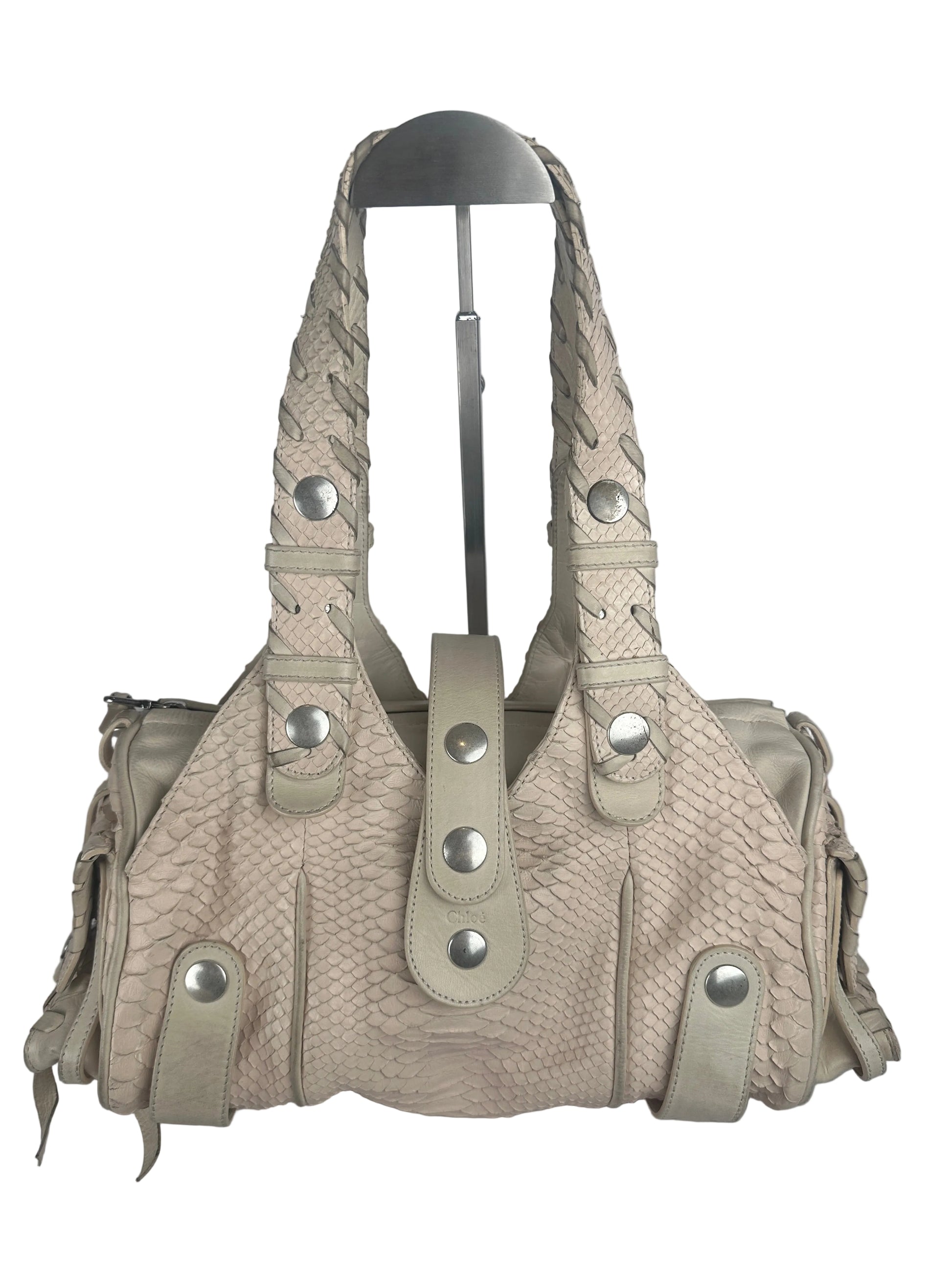 A light beige textured leather shoulder bag with braided strap details and silver-tone snap buttons, shown on a plain light gray background.