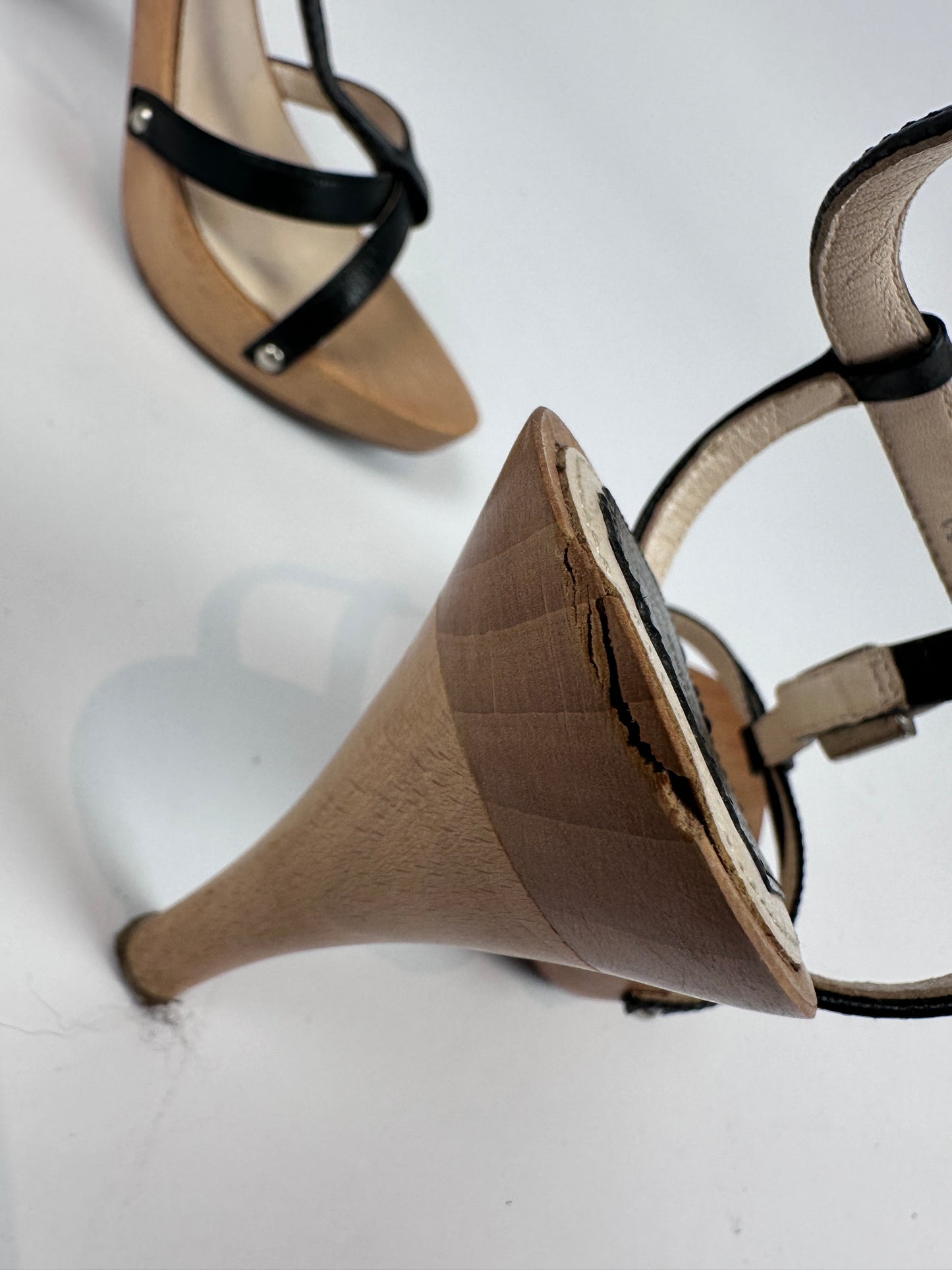 A close-up of a beige platform wedge heel sandal with black straps, showing the sole and heel detail, alongside another view of the sandal on a white background.