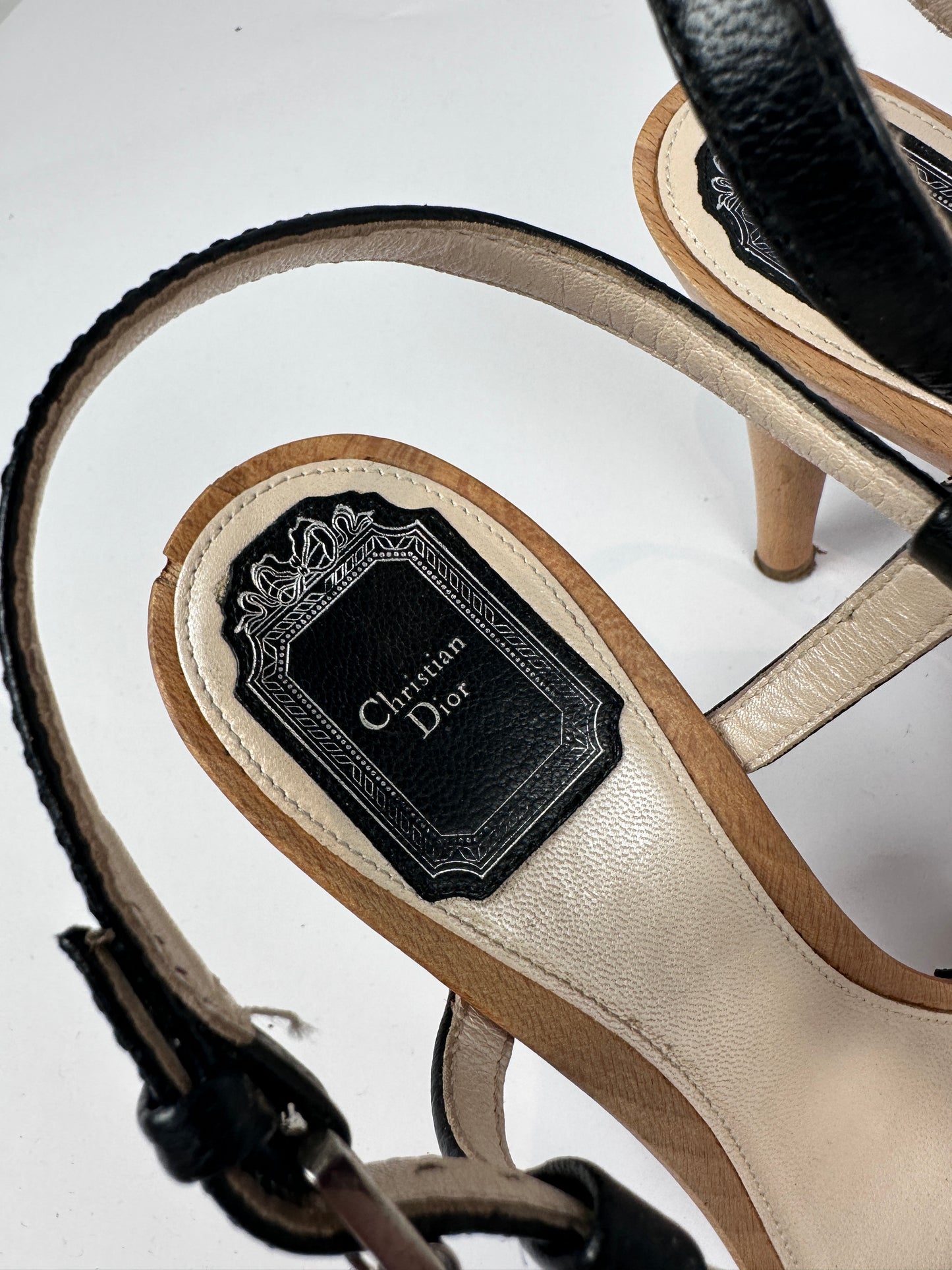 Close-up of a Christian Dior sandal showing the beige leather footbed with a black insole label and black straps on a white background.