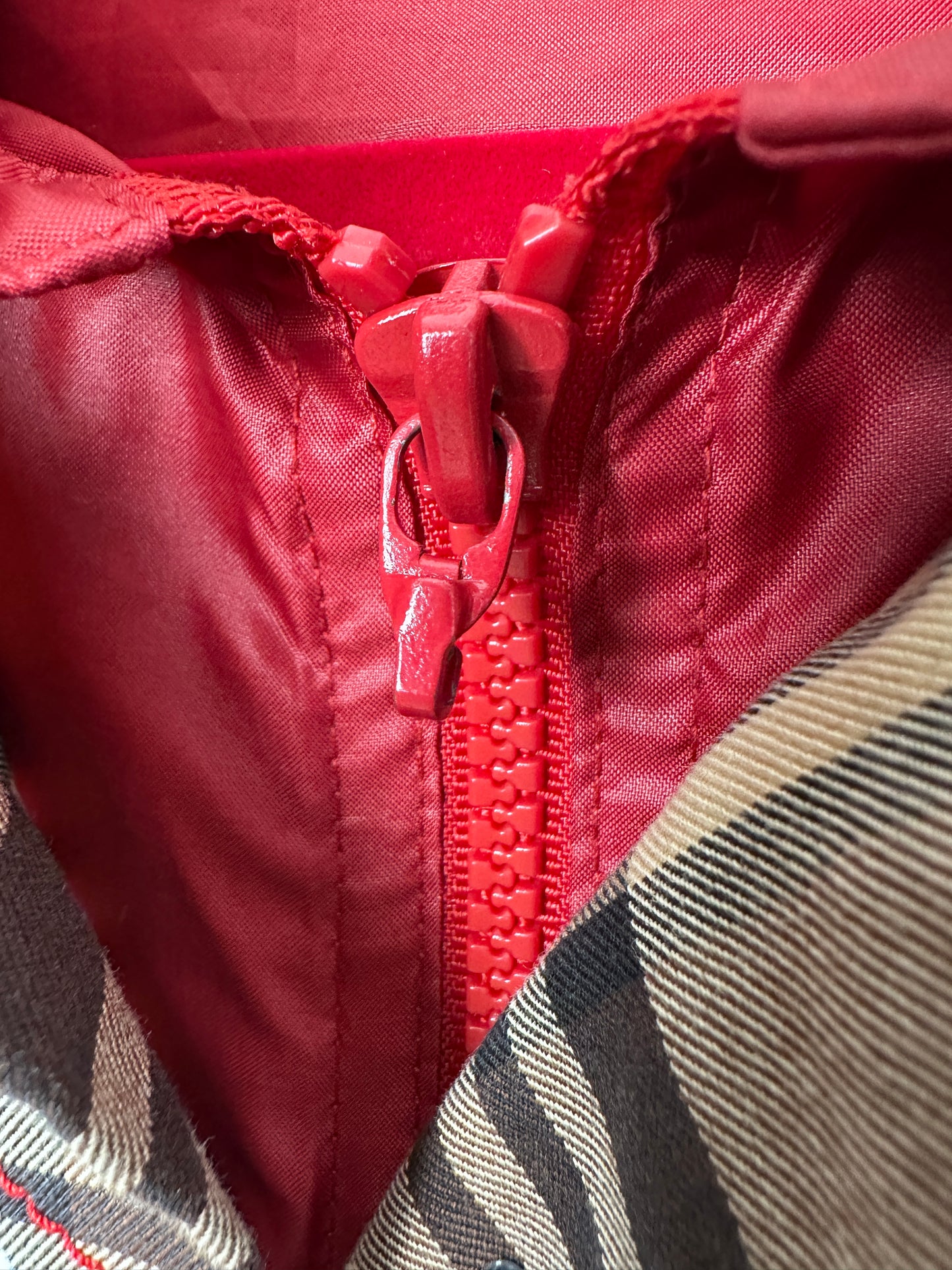 Close-up of a red zipper on a textured fabric surface