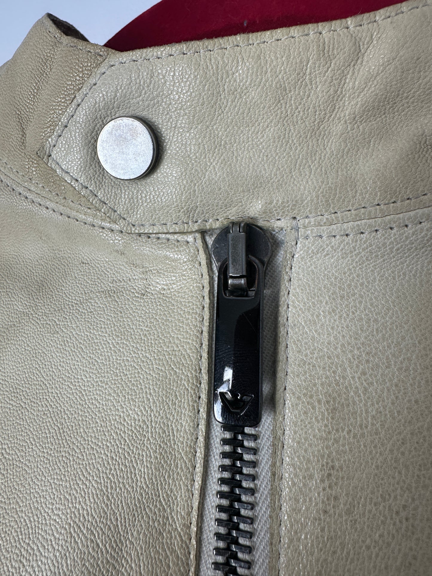 Close-up of a beige leather jacket with a zipper and button detail.