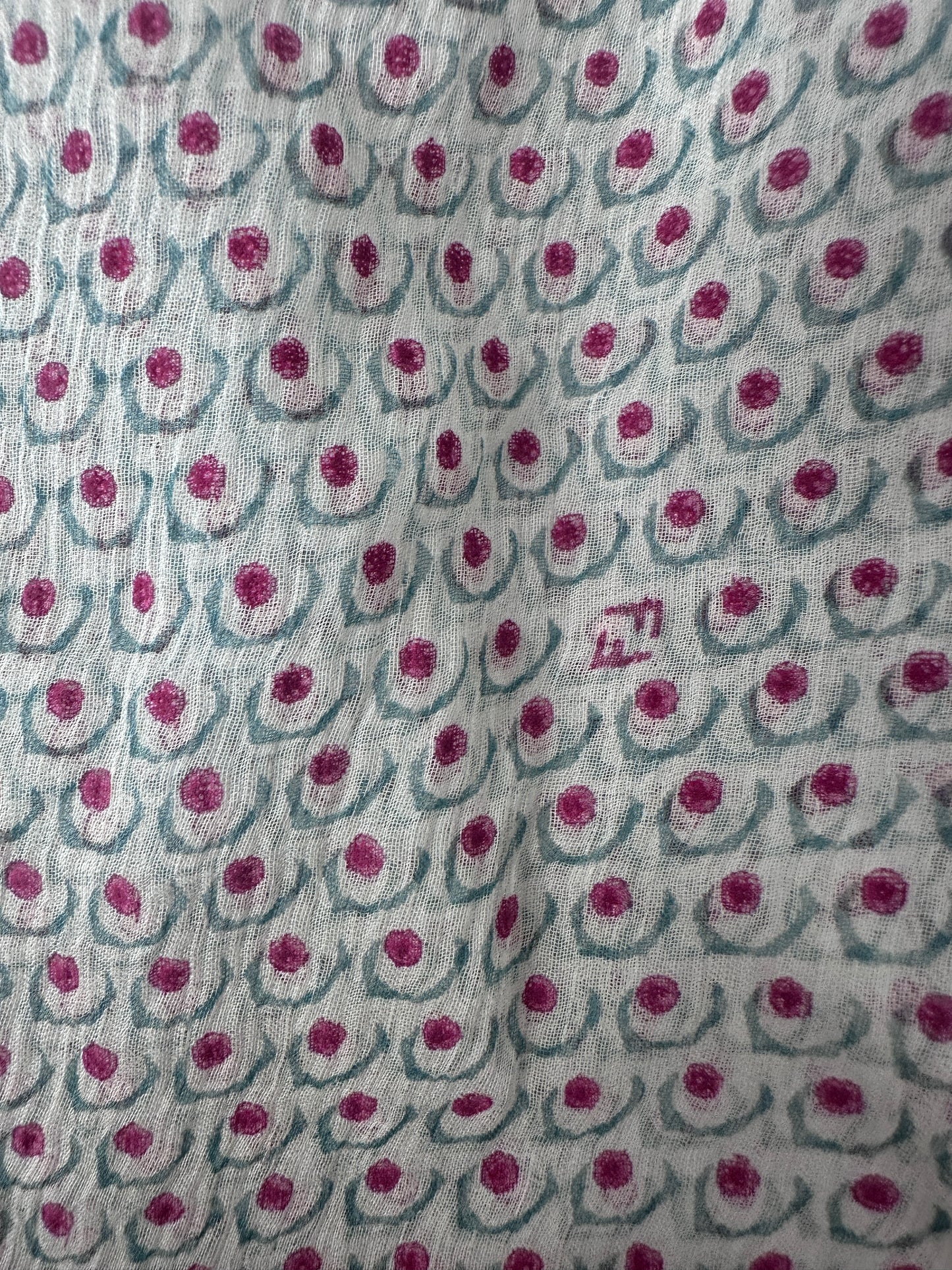 A close-up of a light gray or off-white fabric with a repeating pattern of dusty pink circular motifs and muted blue-gray curved lines.