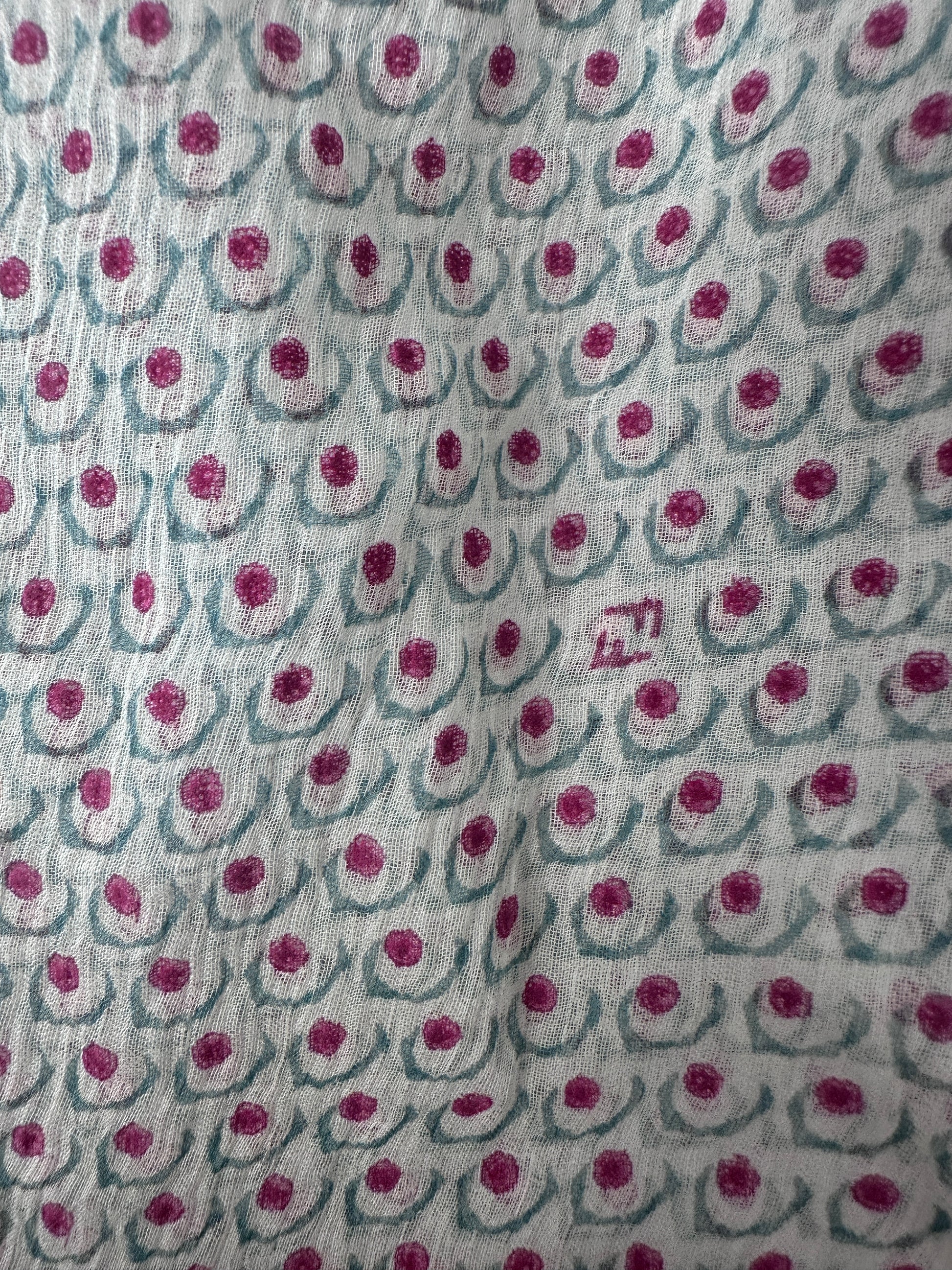 A close-up of a light gray or off-white fabric with a repeating pattern of dusty pink circular motifs and muted blue-gray curved lines.