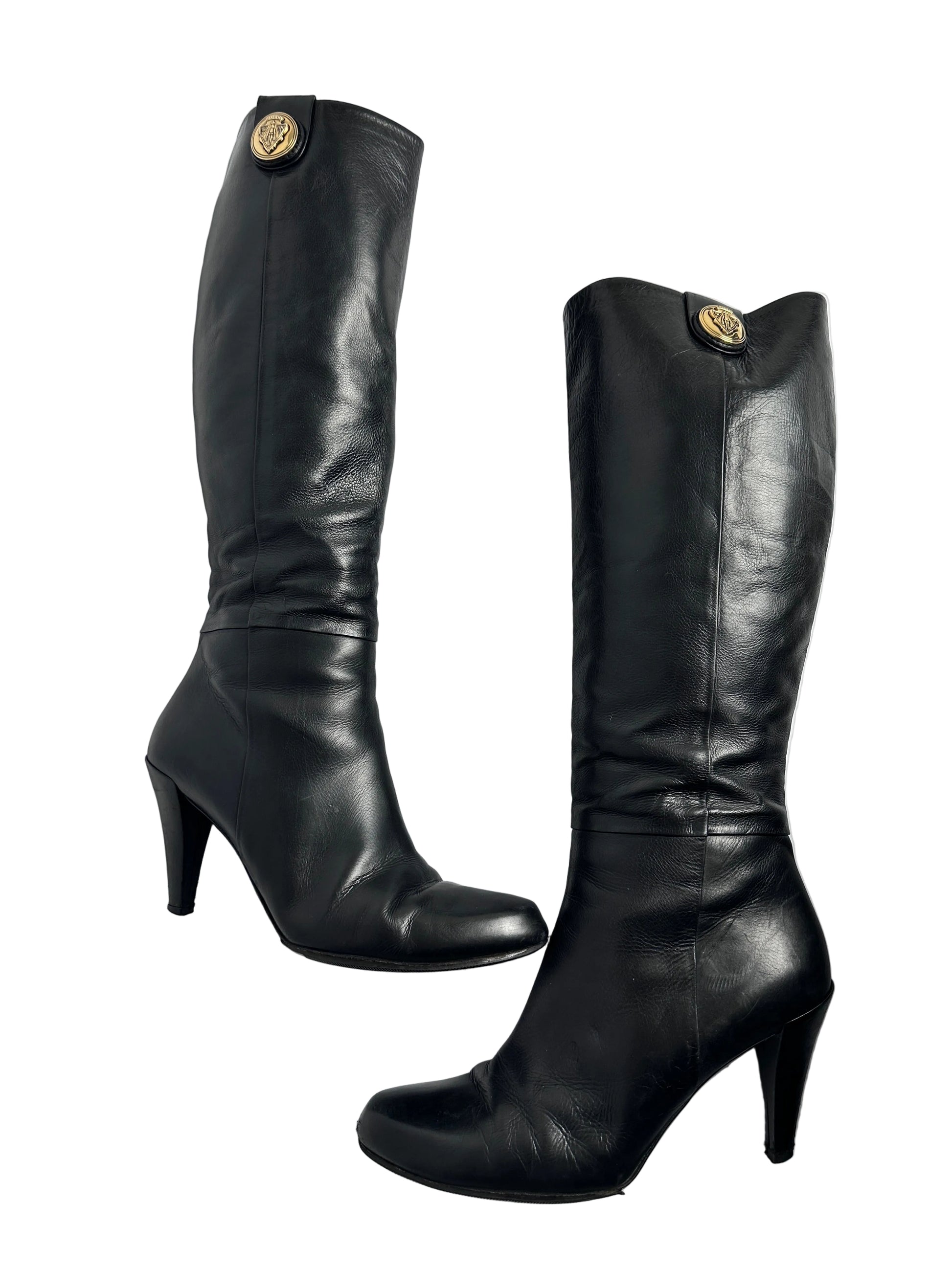 Pair of black leather knee-high boots with gold buttons on a white background