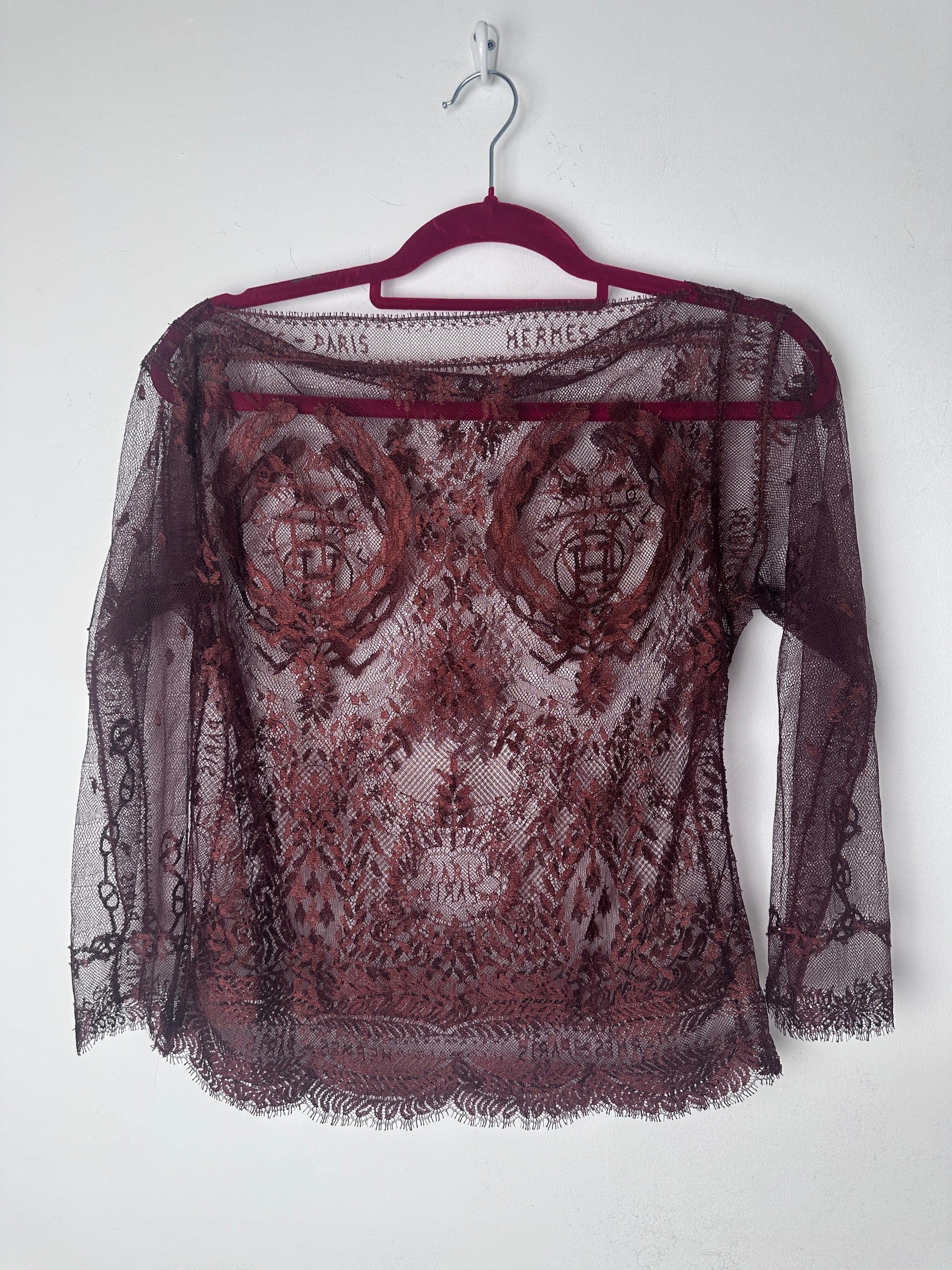 A sheer burgundy lace shawl with a floral pattern and fringed edges, draped over a matching burgundy hanger against a plain white background.