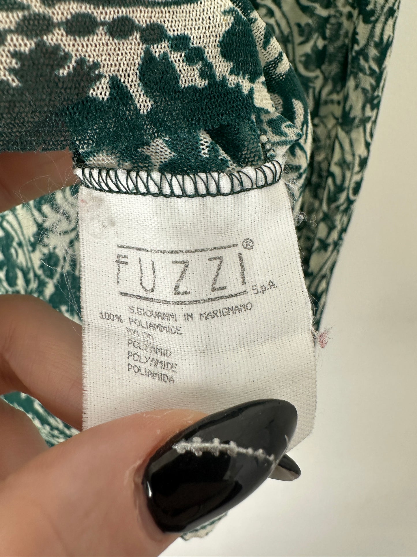 Close-up of a patterned fabric with a 'FUZZI' label held by a hand.