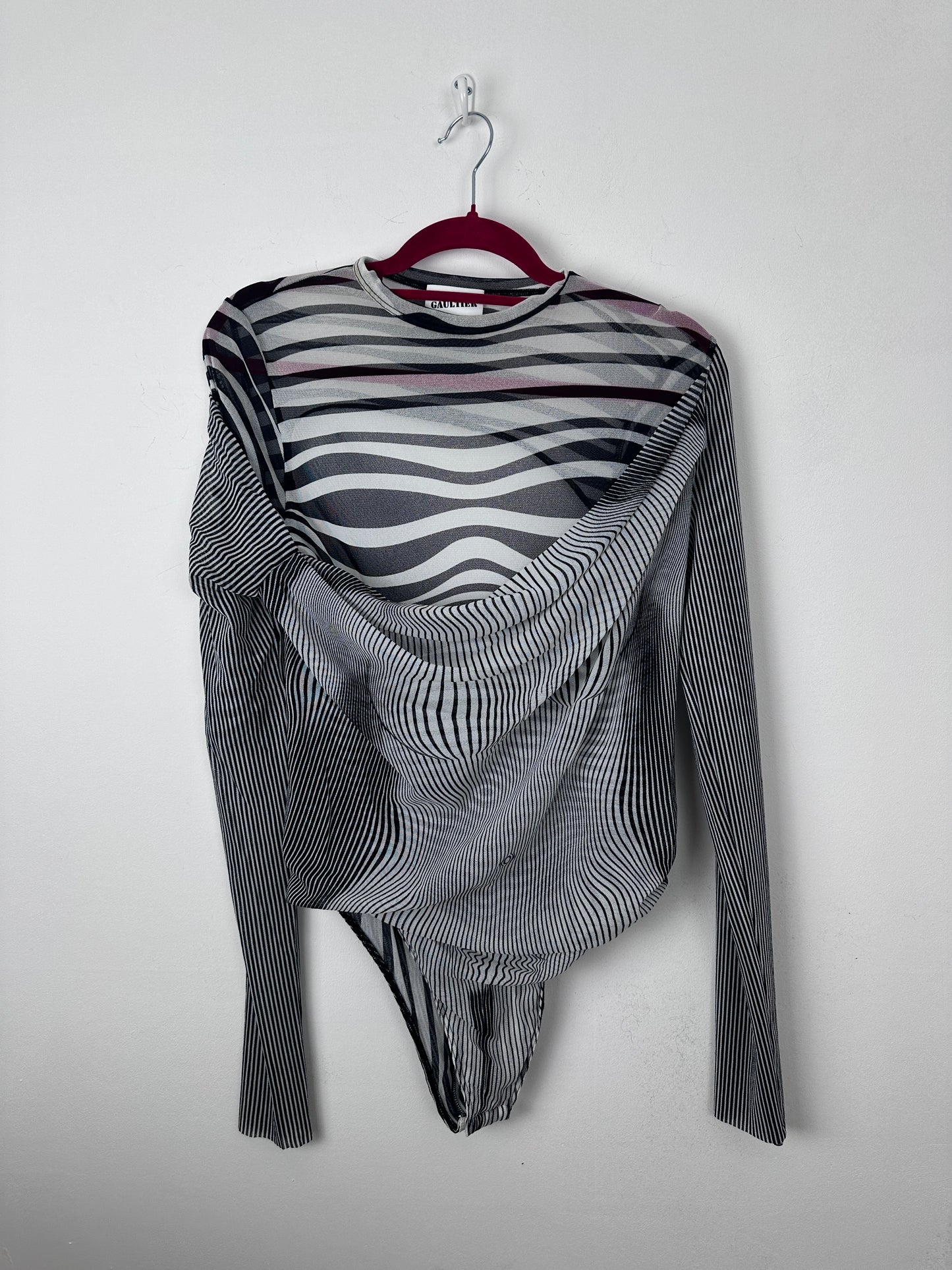 A long-sleeve striped knit top with black, white, and gray wavy patterns, draped on a red hanger against a plain light gray background.