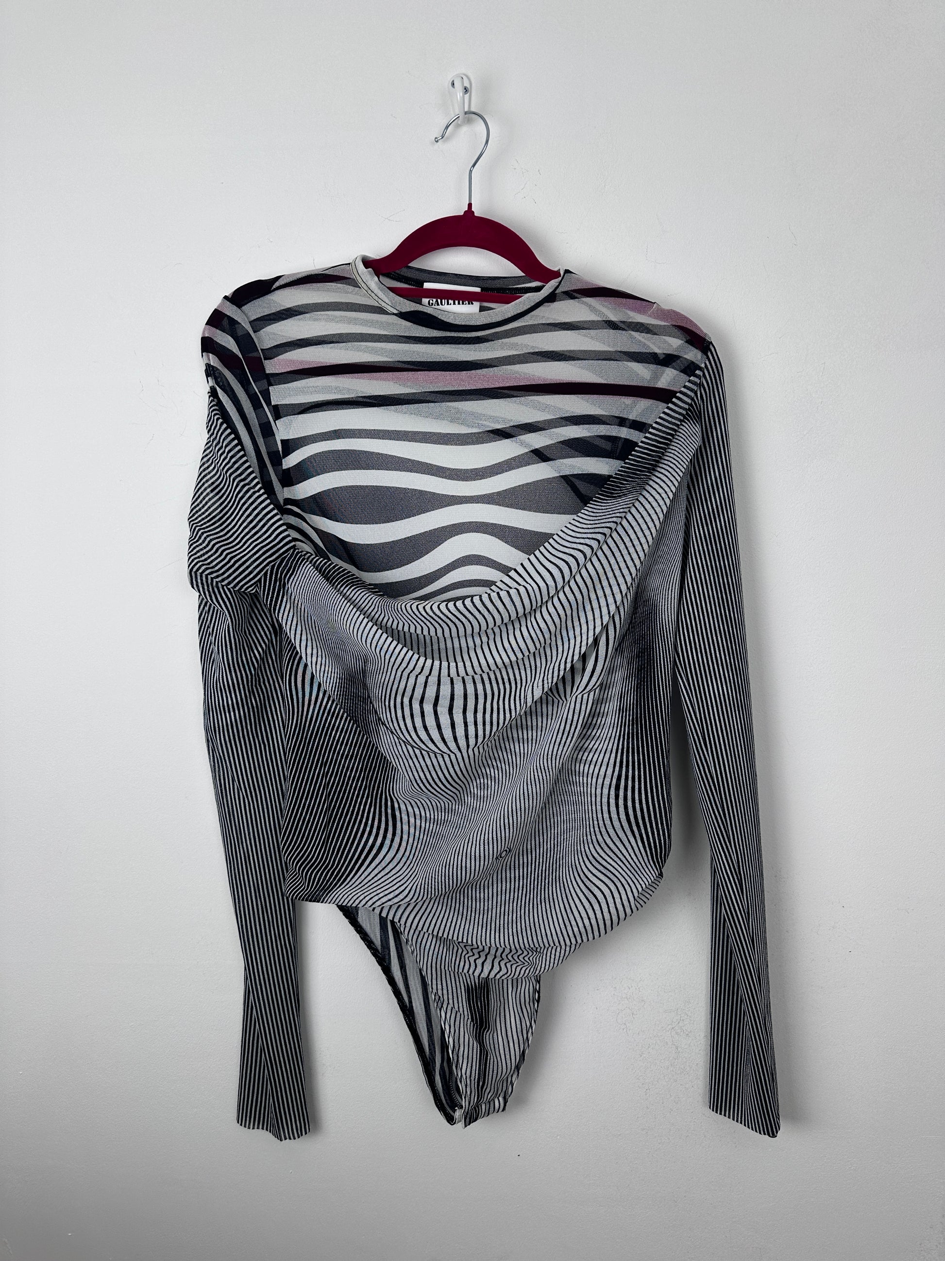 A long-sleeve striped knit top with black, white, and gray wavy patterns, draped on a red hanger against a plain light gray background.