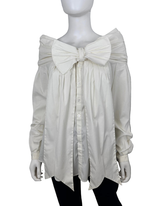 An oversized white long-sleeve shirt dress with a large bow at the waist and a button-down front, displayed on a white mannequin against a light gray background.