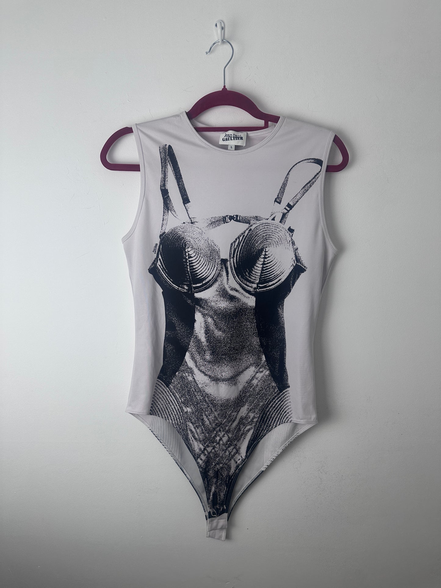 A sleeveless white tank top with a large black and white graphic print of a butterfly on the front, hanging on a dark purple hanger against a plain light gray wall.