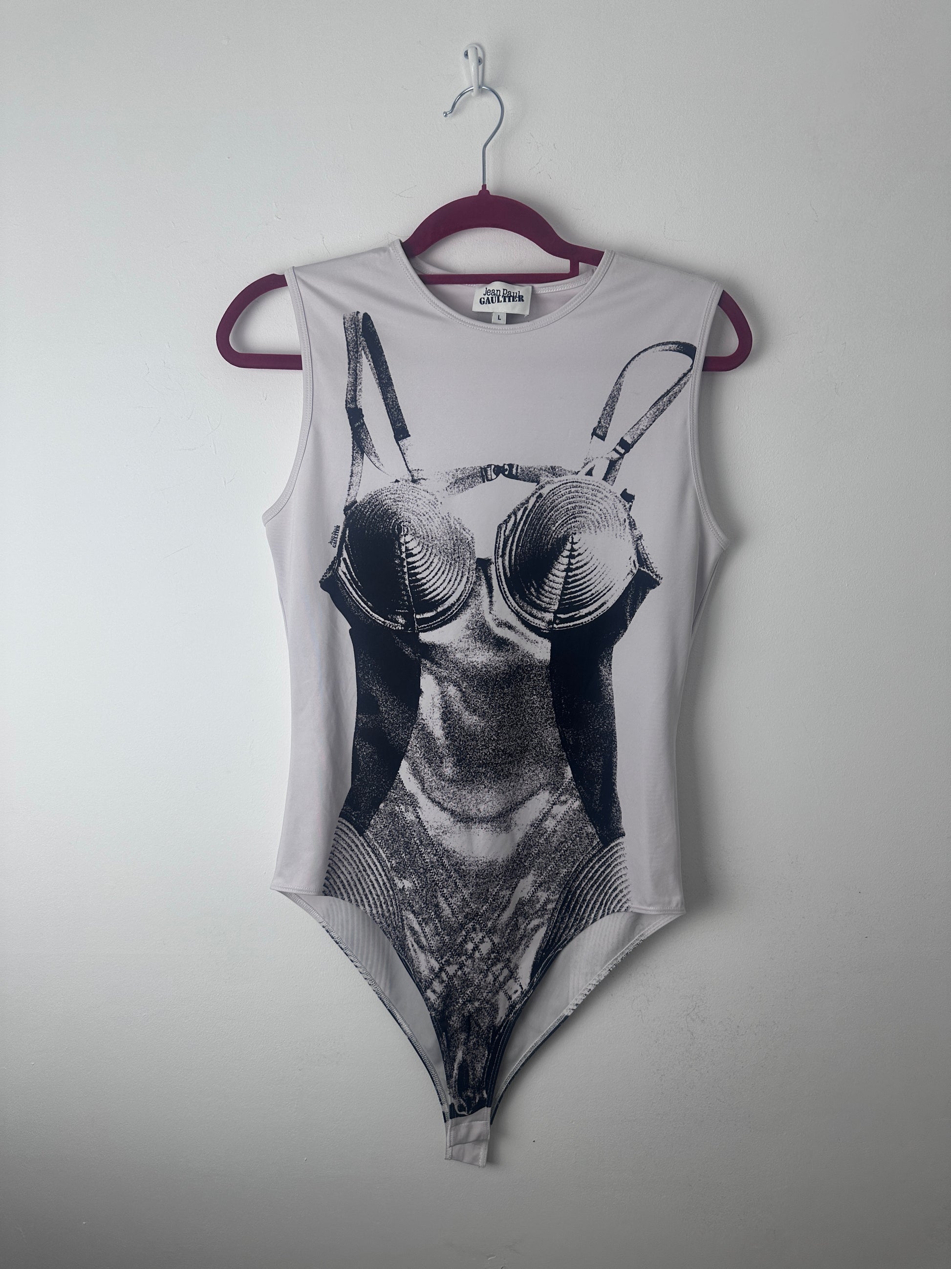 A sleeveless white tank top with a large black and white graphic print of a butterfly on the front, hanging on a dark purple hanger against a plain light gray wall.