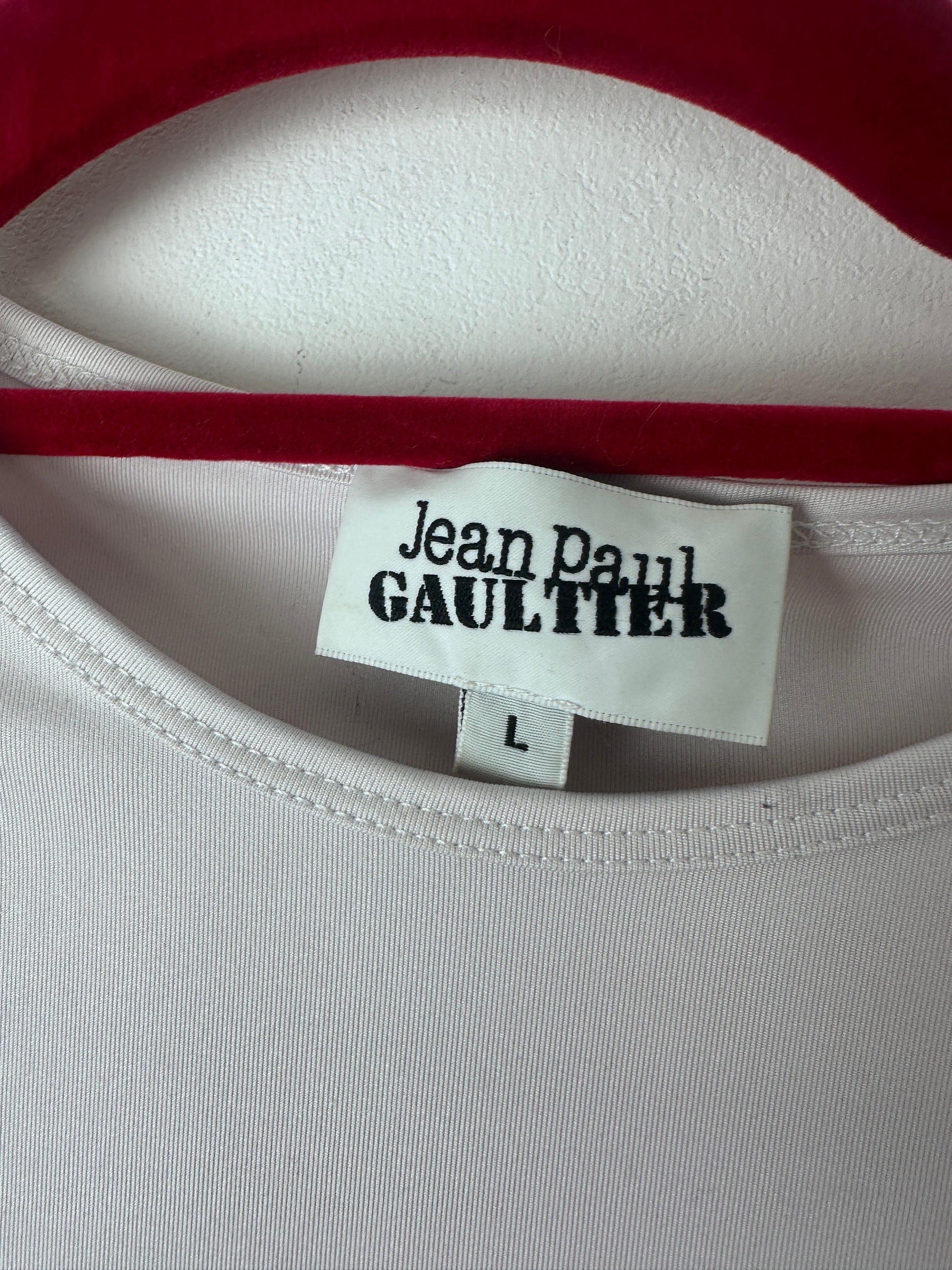 Close-up of a white garment neck label reading 'Jean Paul Gaultier' with a size 'L', next to a red trim and white fabric.