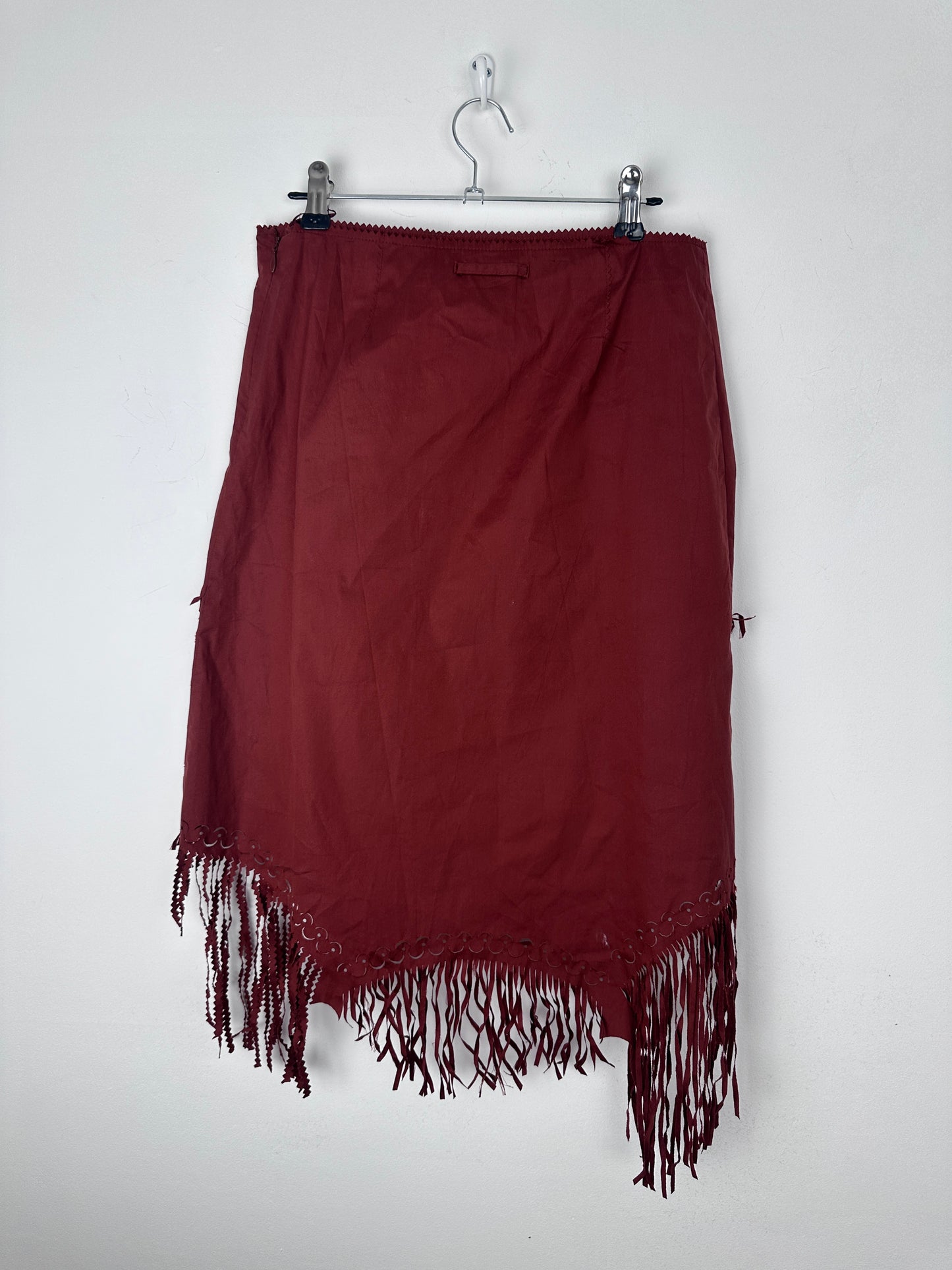A dark burgundy skirt with fringe trim, hanging from a metal hanger against a plain white background.