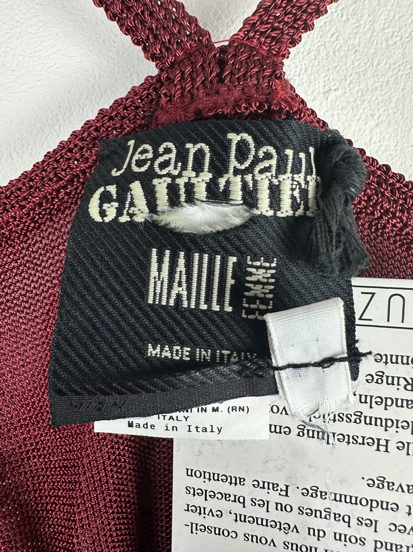 Close-up of a burgundy belt with 'Jean Paul Gaultier' label on a white background