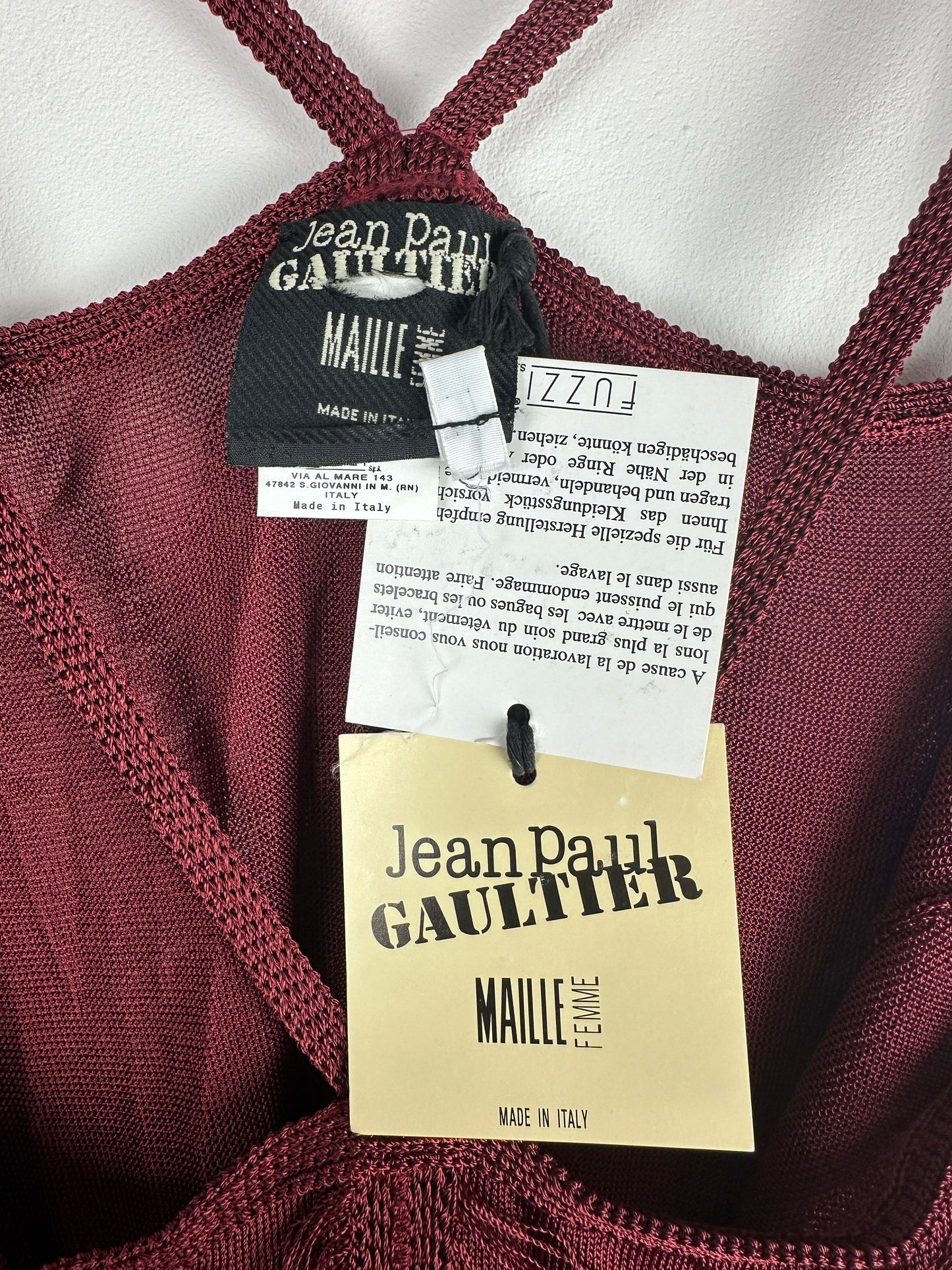Close-up of a maroon garment with 'Jean Paul Gaultier' tags on a white background