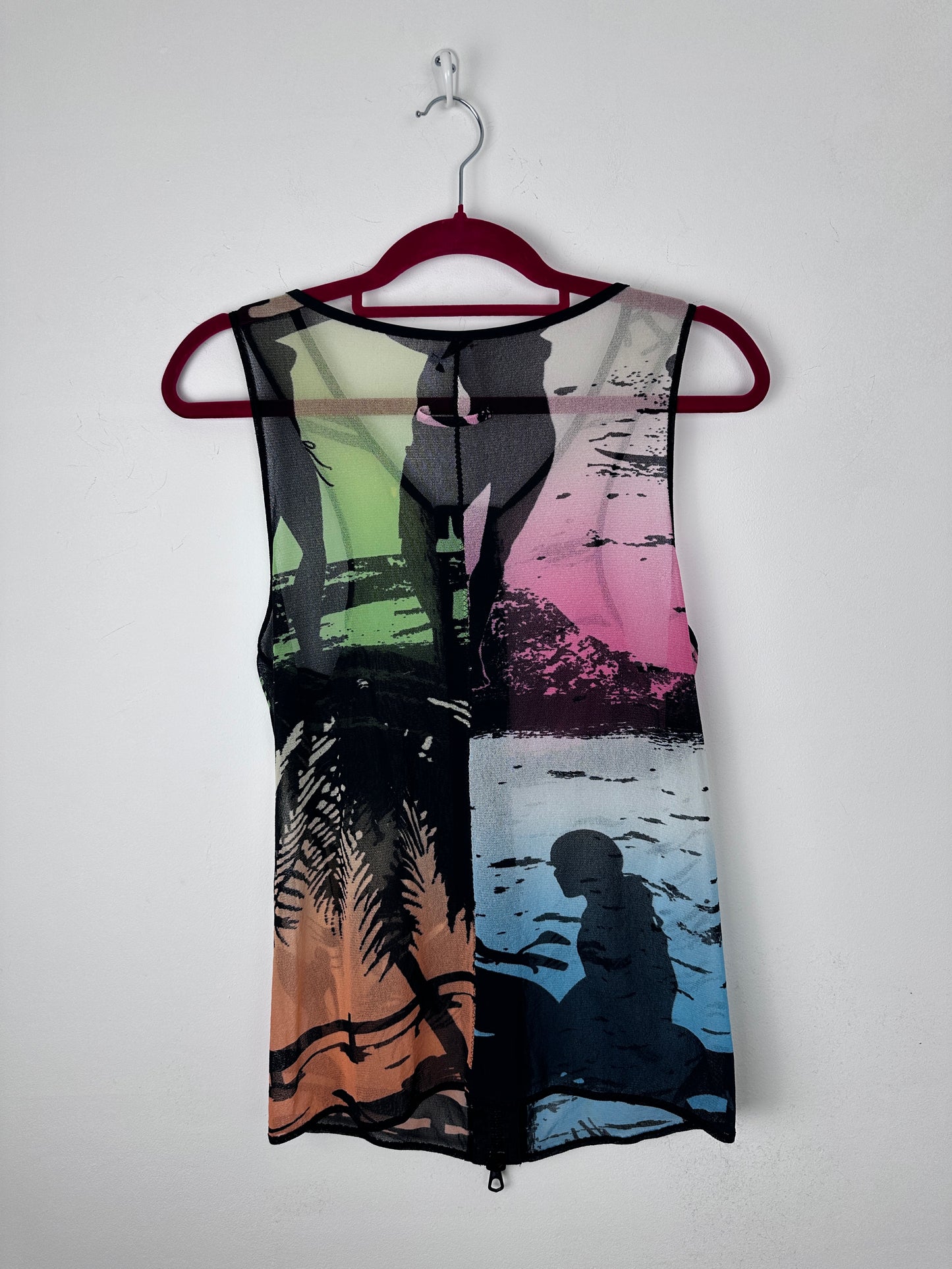 A sleeveless sheer mesh top with a multicolor abstract print, hanging on a dark red hanger against a plain white wall.