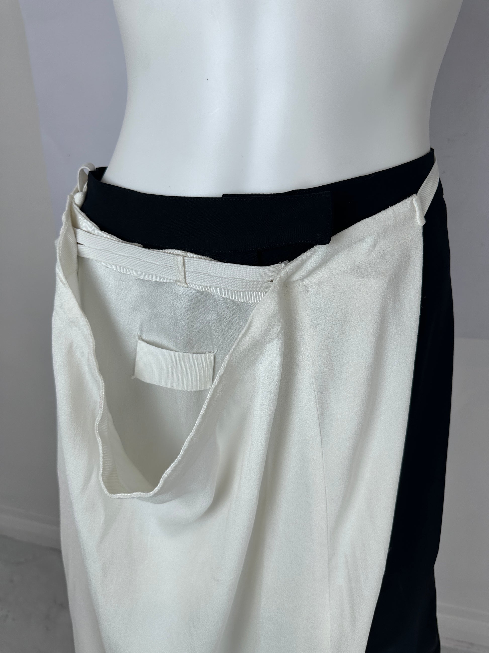 A close-up of a white garment displayed on a white mannequin torso, showing a black waistband or inner layer and a small white fabric tab near the center.