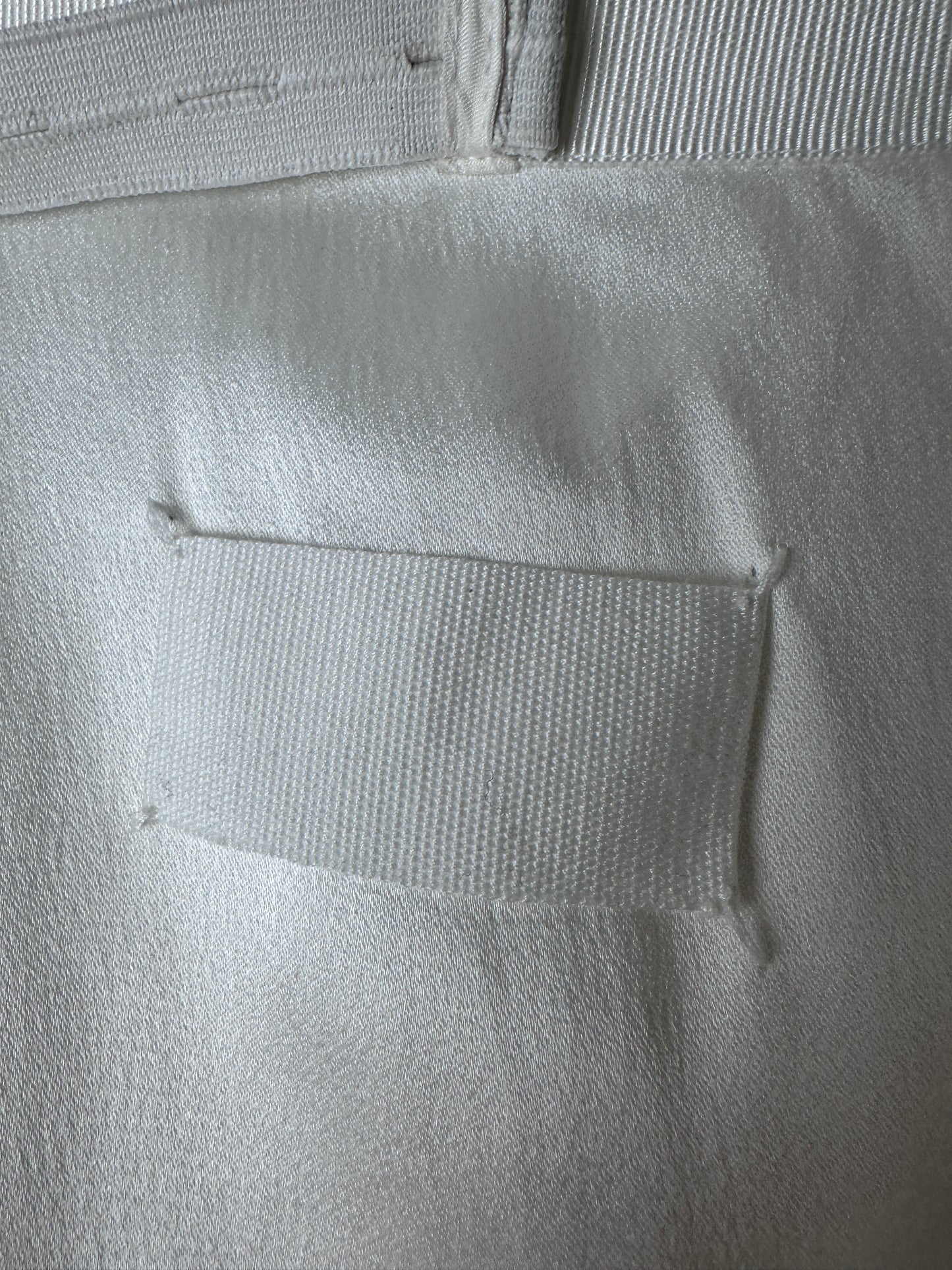 Close-up of a white textured fabric item with a rectangular hook-and-loop patch and a striped fabric strip on the left side.