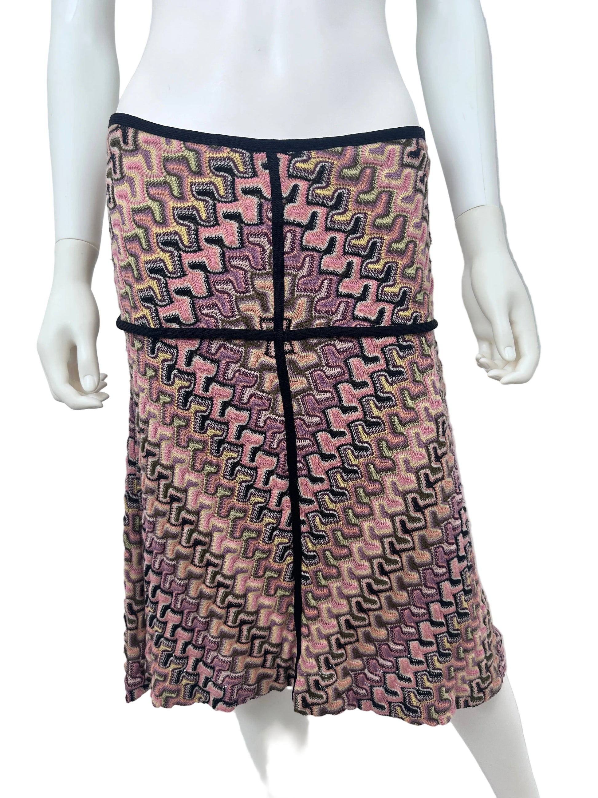 A folded skirt with a pink, purple, and black geometric pattern, displayed on a white mannequin torso against a white wall.
