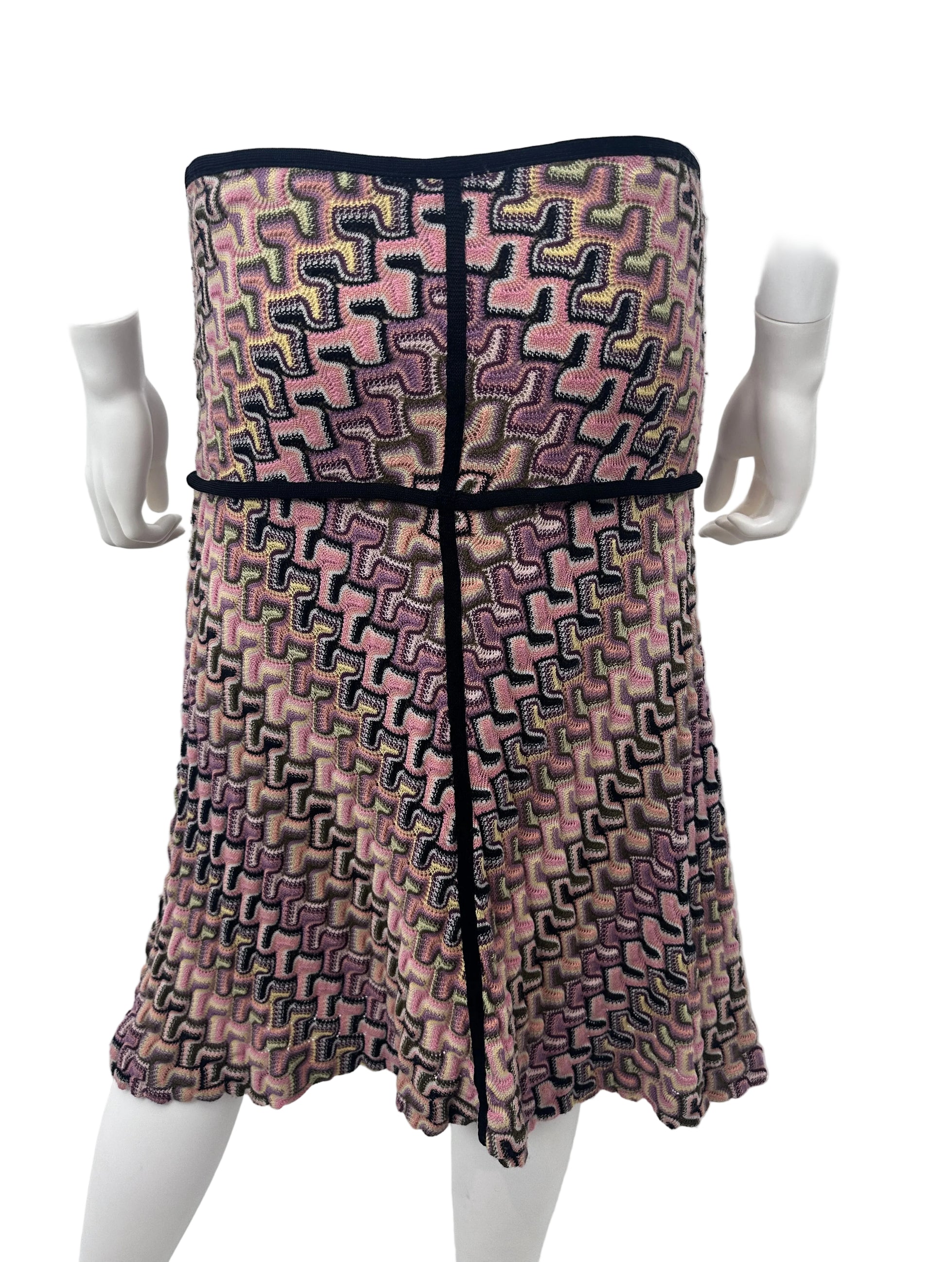 A patterned knit dress displayed on a white mannequin torso, featuring a geometric maze-like weave in pink, purple, black, and beige tones with solid black trim.