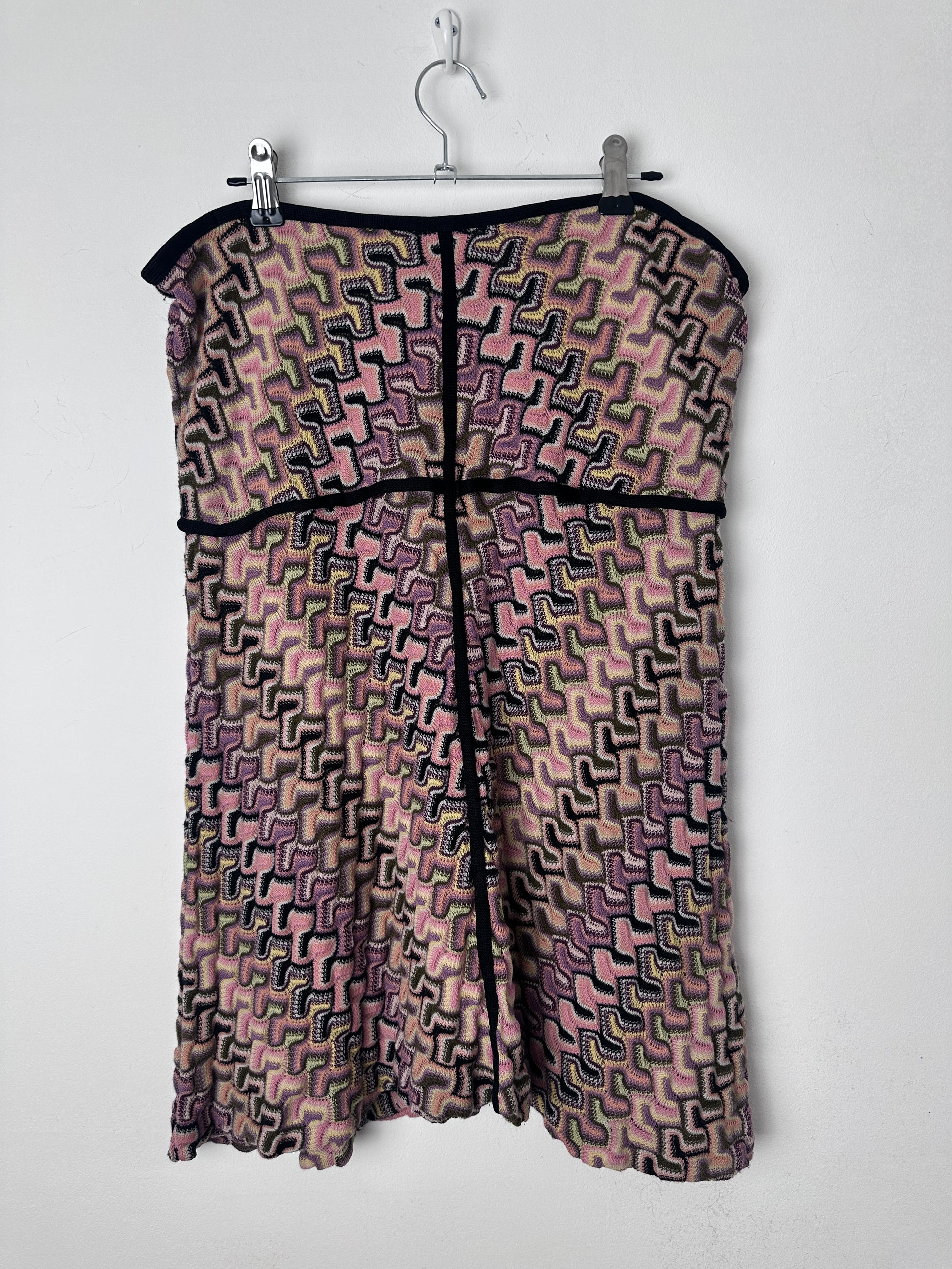 A folded patterned fabric garment or textile piece with a geometric maze-like print in pink, purple, black, and beige tones, shown on a white hanger against a white background.