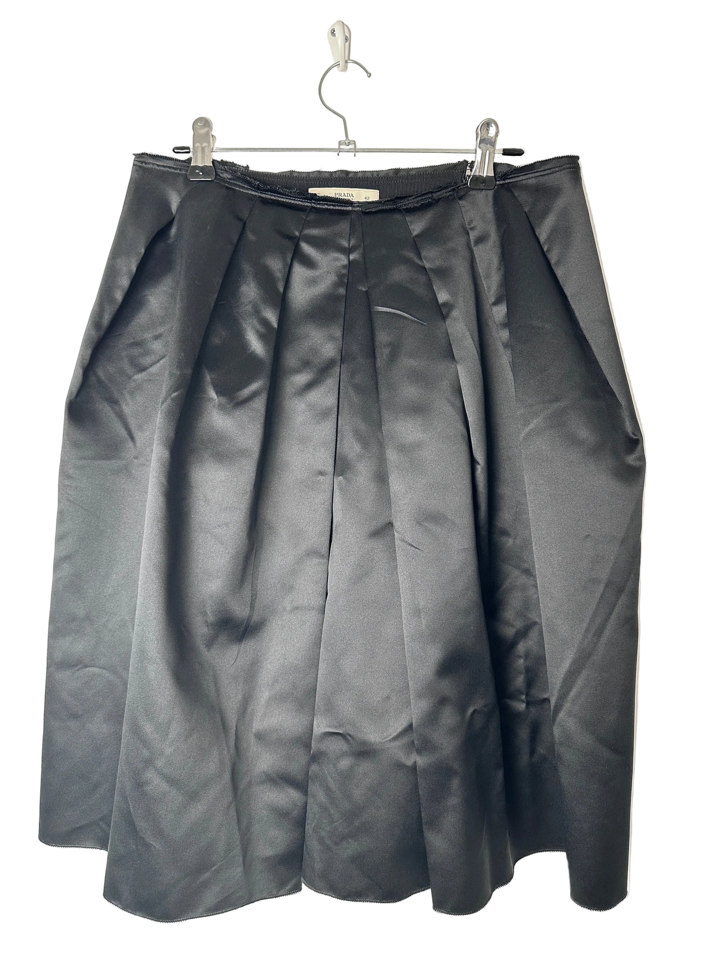 Folded black skirt on a clear hanger against a beige background