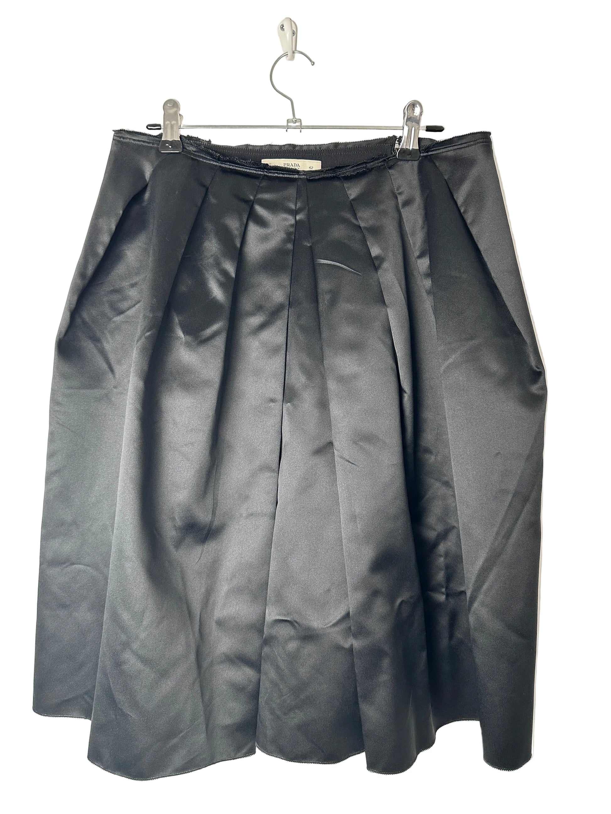 Folded black skirt on a clear hanger against a beige background