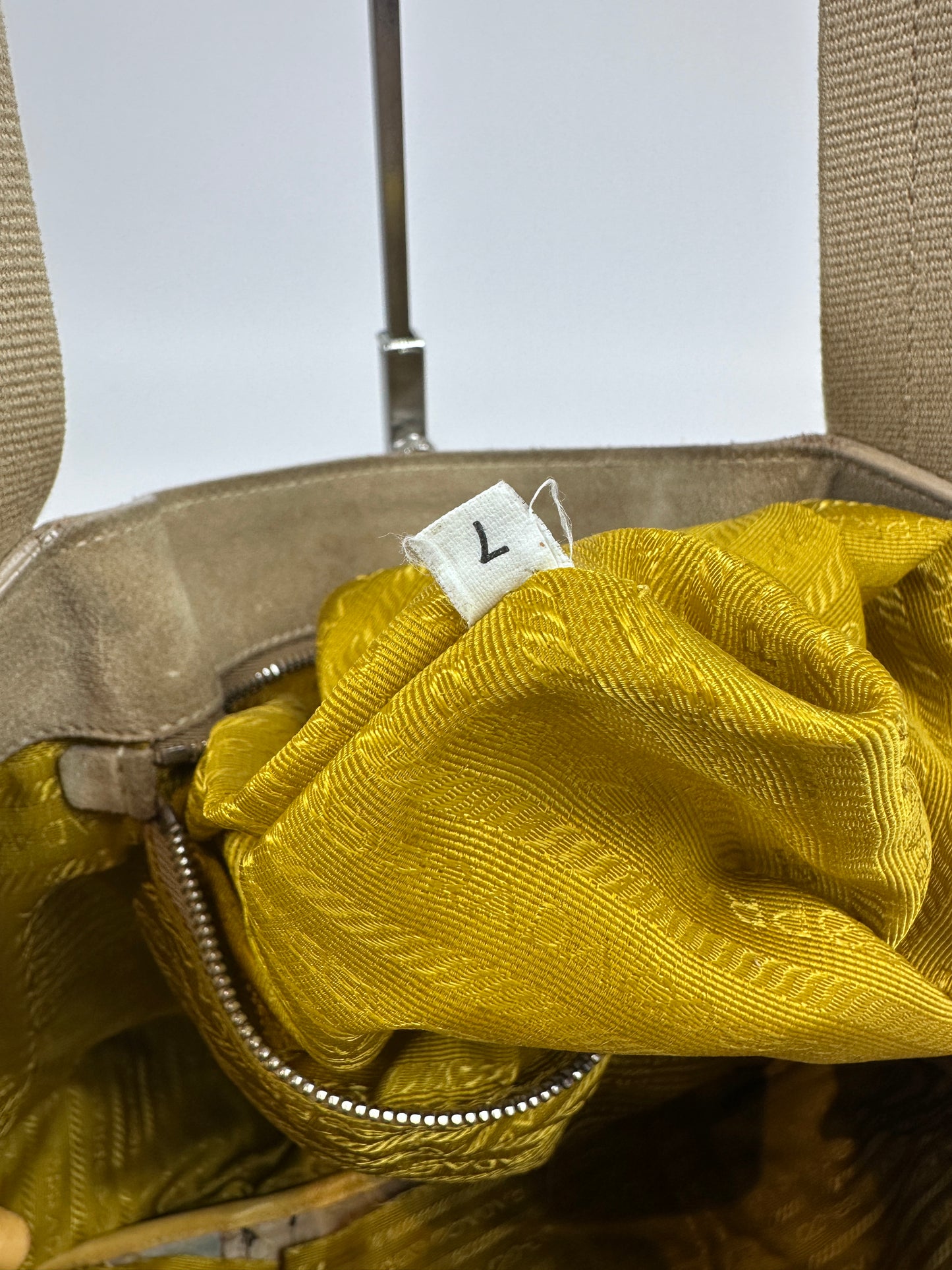 Close-up of a beige handbag interior with a textured mustard yellow fabric lining and a white size tag marked with the number 7.