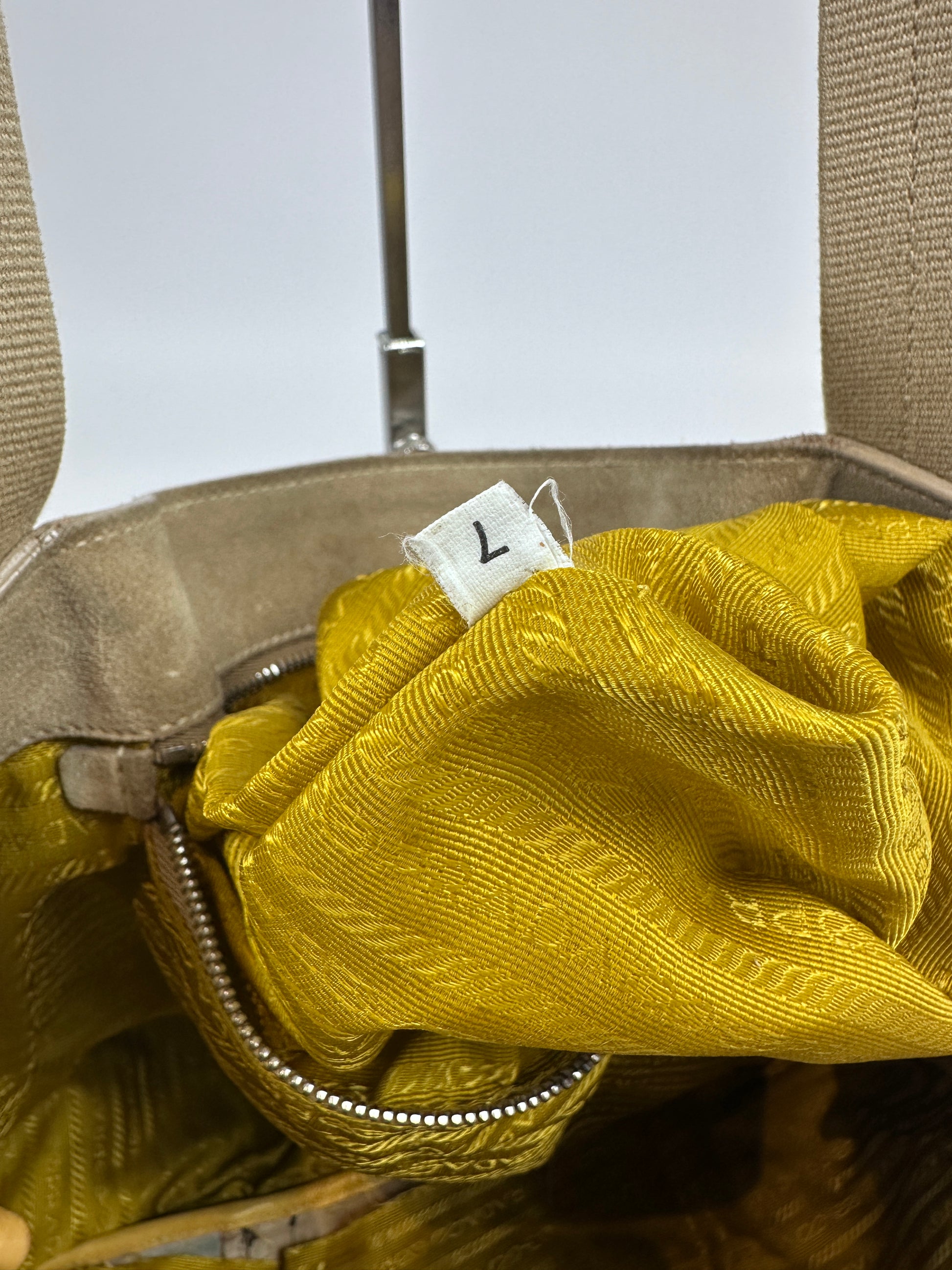 Close-up of a beige handbag interior with a textured mustard yellow fabric lining and a white size tag marked with the number 7.