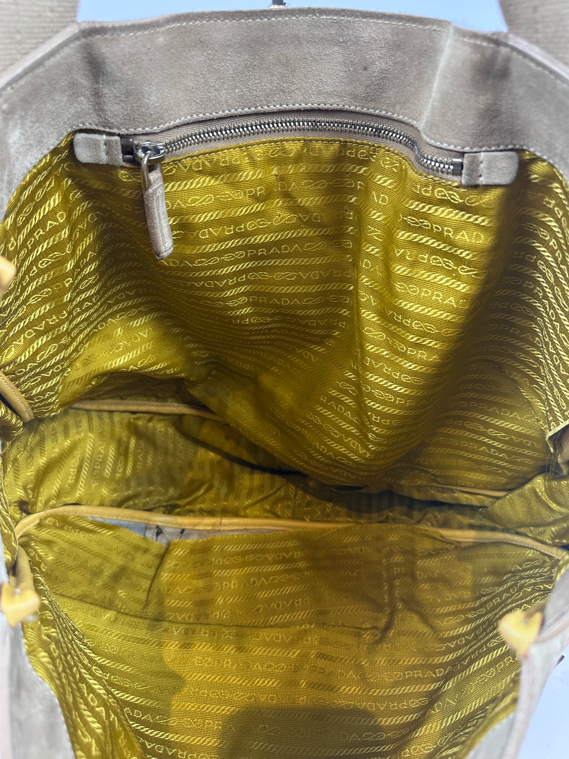 Close-up of the interior of a handbag showing a metallic gold patterned lining with a zipper pocket and gray fabric trim.