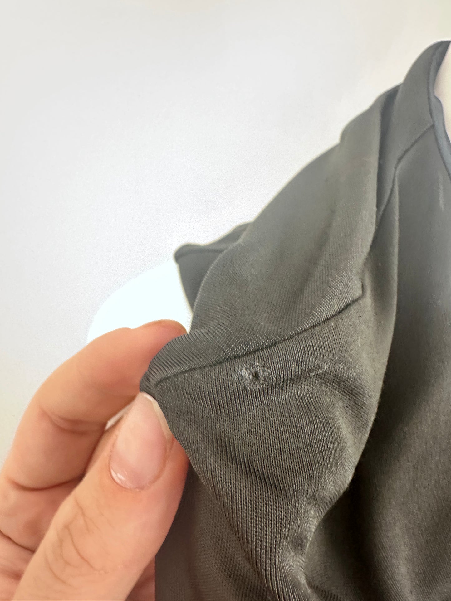 Close-up of a person's hand holding up a dark gray ribbed fabric garment, showing the texture and a small hole or snag on the sleeve.