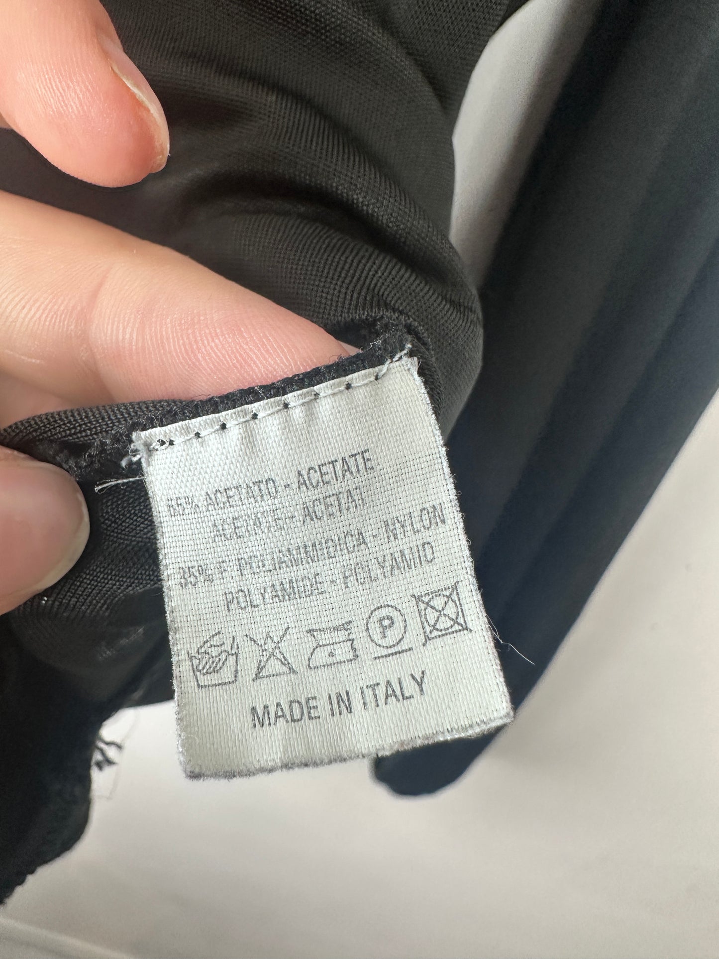 Close-up of a black garment label held by fingers, showing care instructions and 'MADE IN ITALY' text on a white fabric tag.