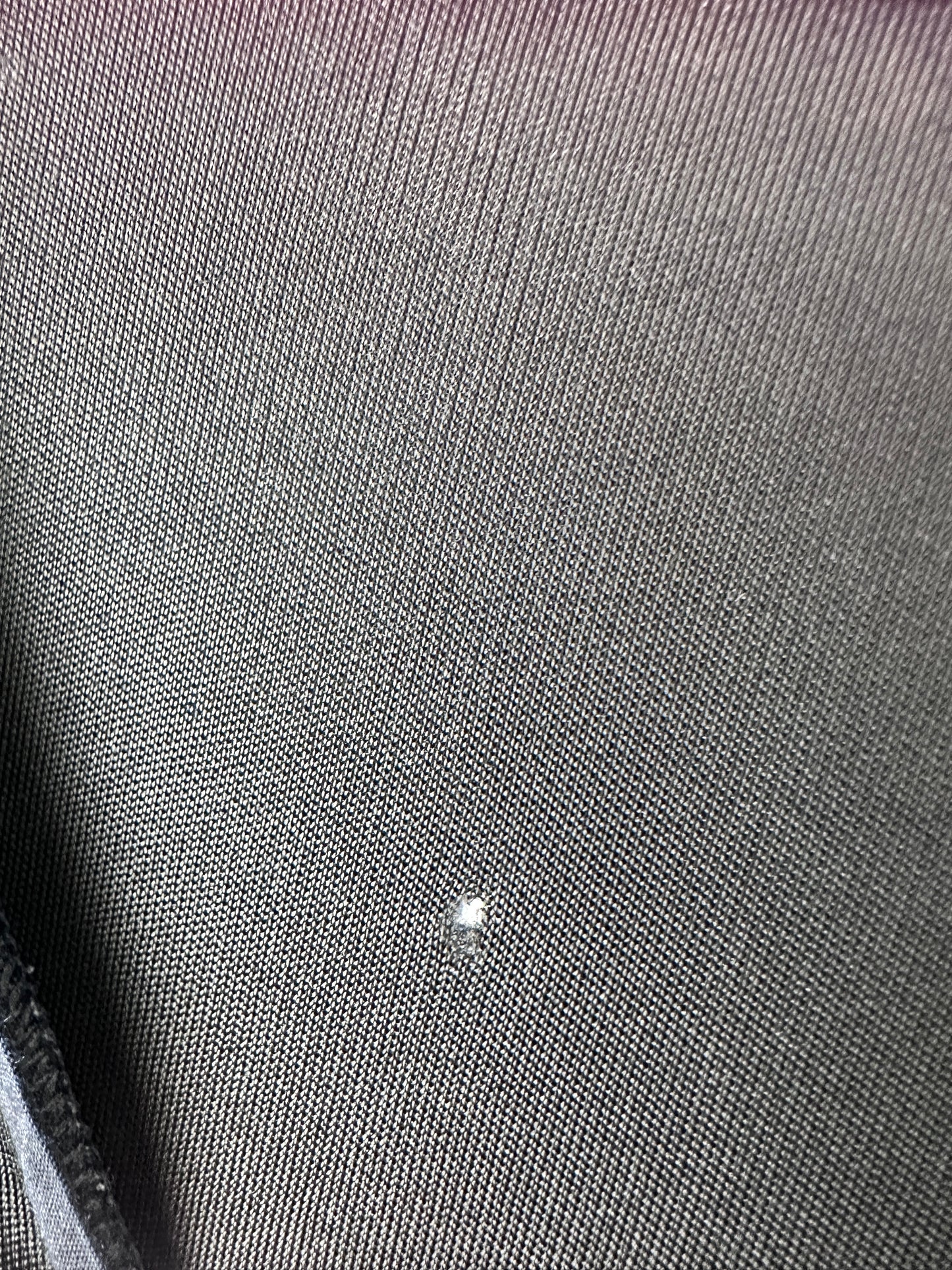 Close-up of a dark gray textured fabric surface with a small white speck or glare near the center-right.