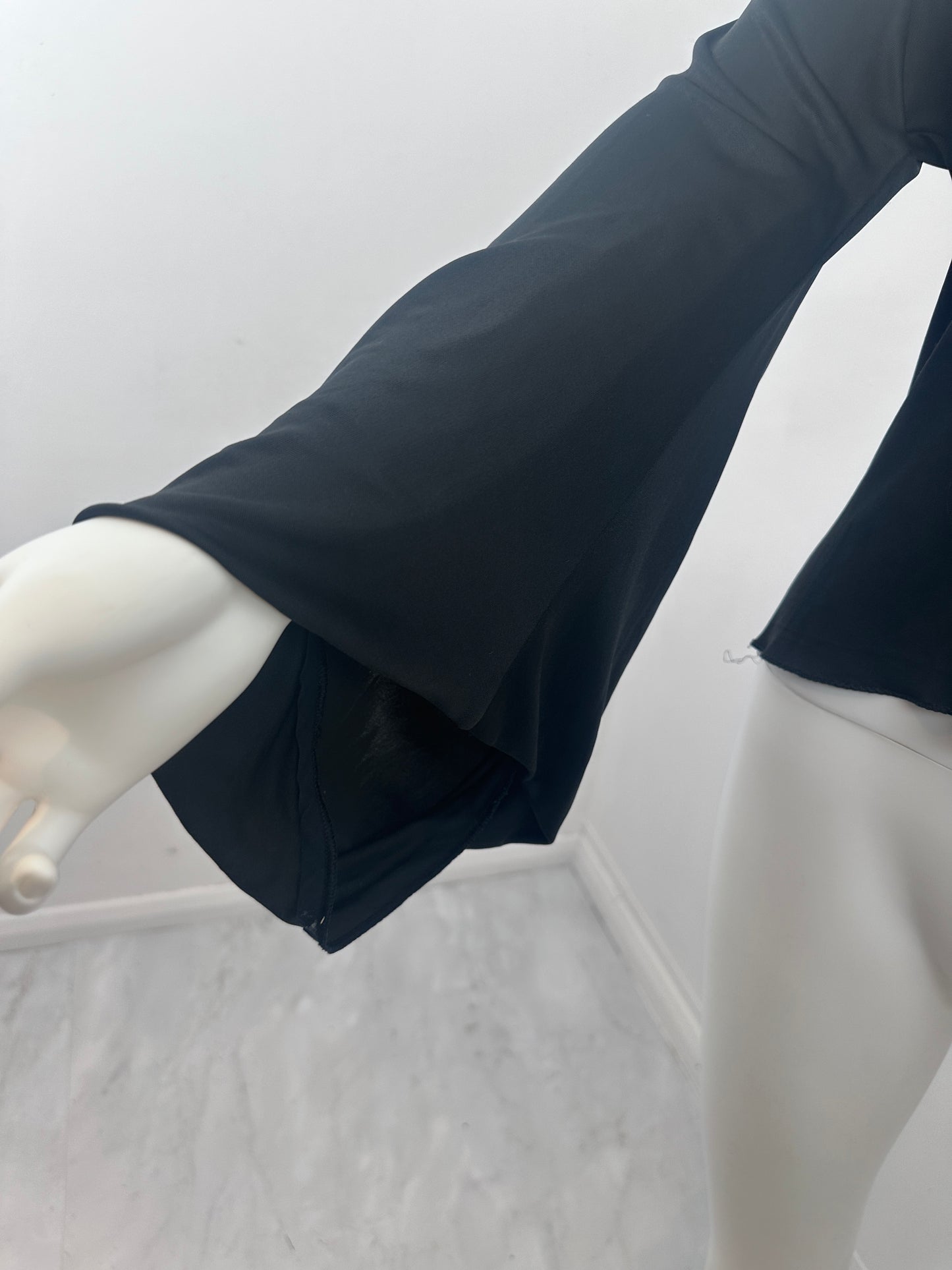 Close-up of a black sleeveless top or dress displayed on a white mannequin, showing the fabric drape and a gathered side seam against a white background.