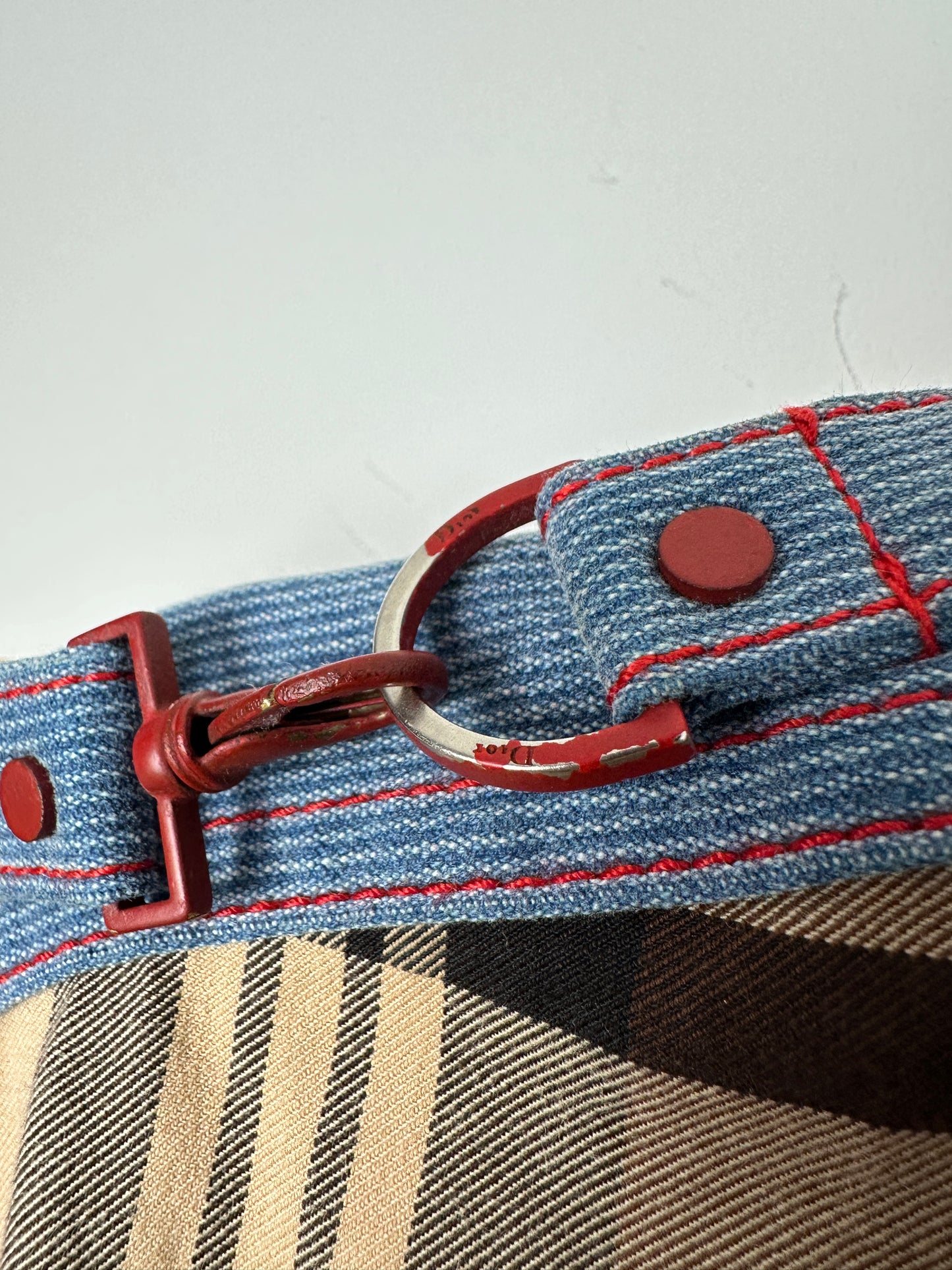 Close-up of a denim strap with red stitching and hardware on a checkered fabric background.