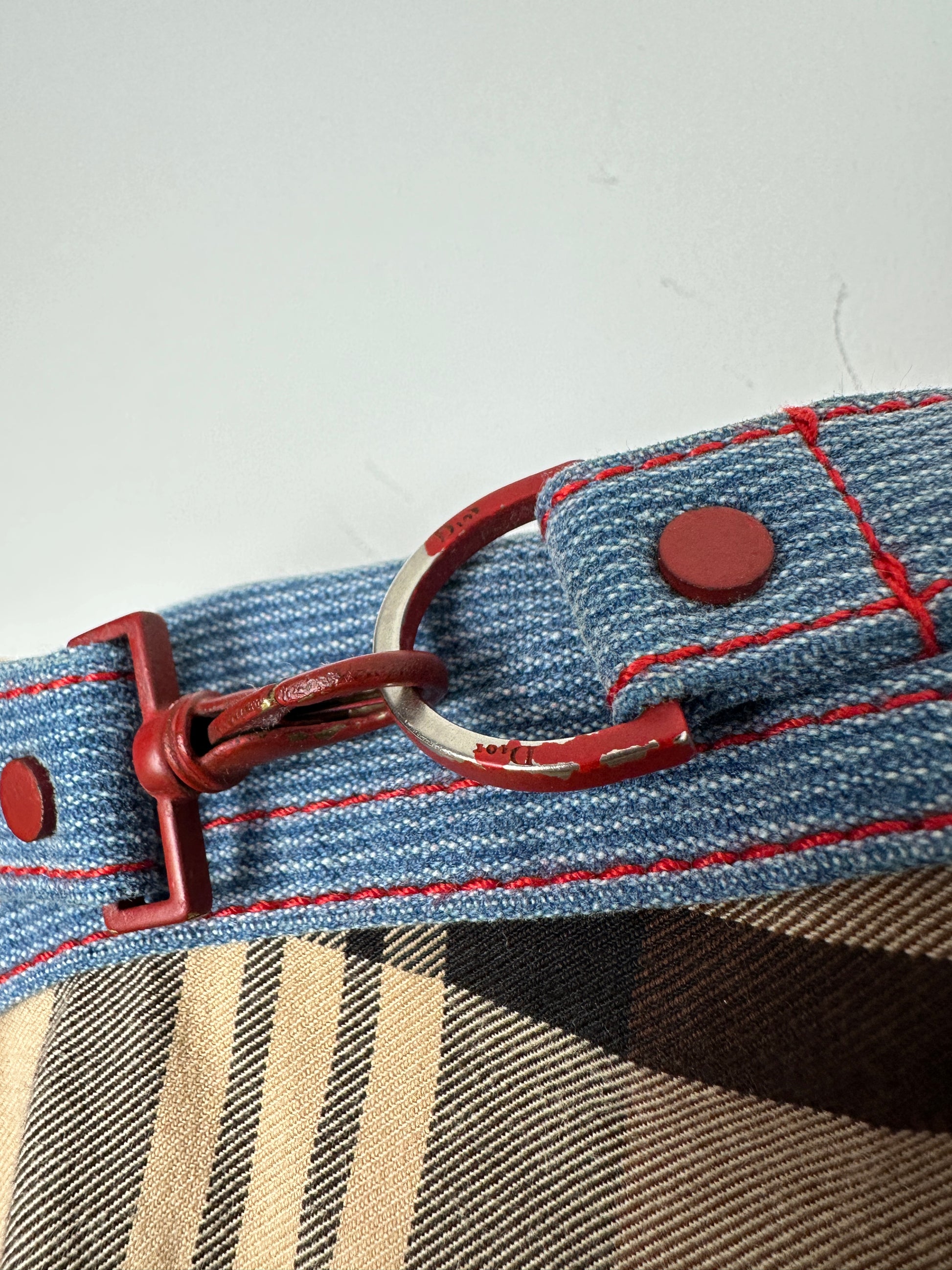 Close-up of a denim strap with red stitching and hardware on a checkered fabric background.