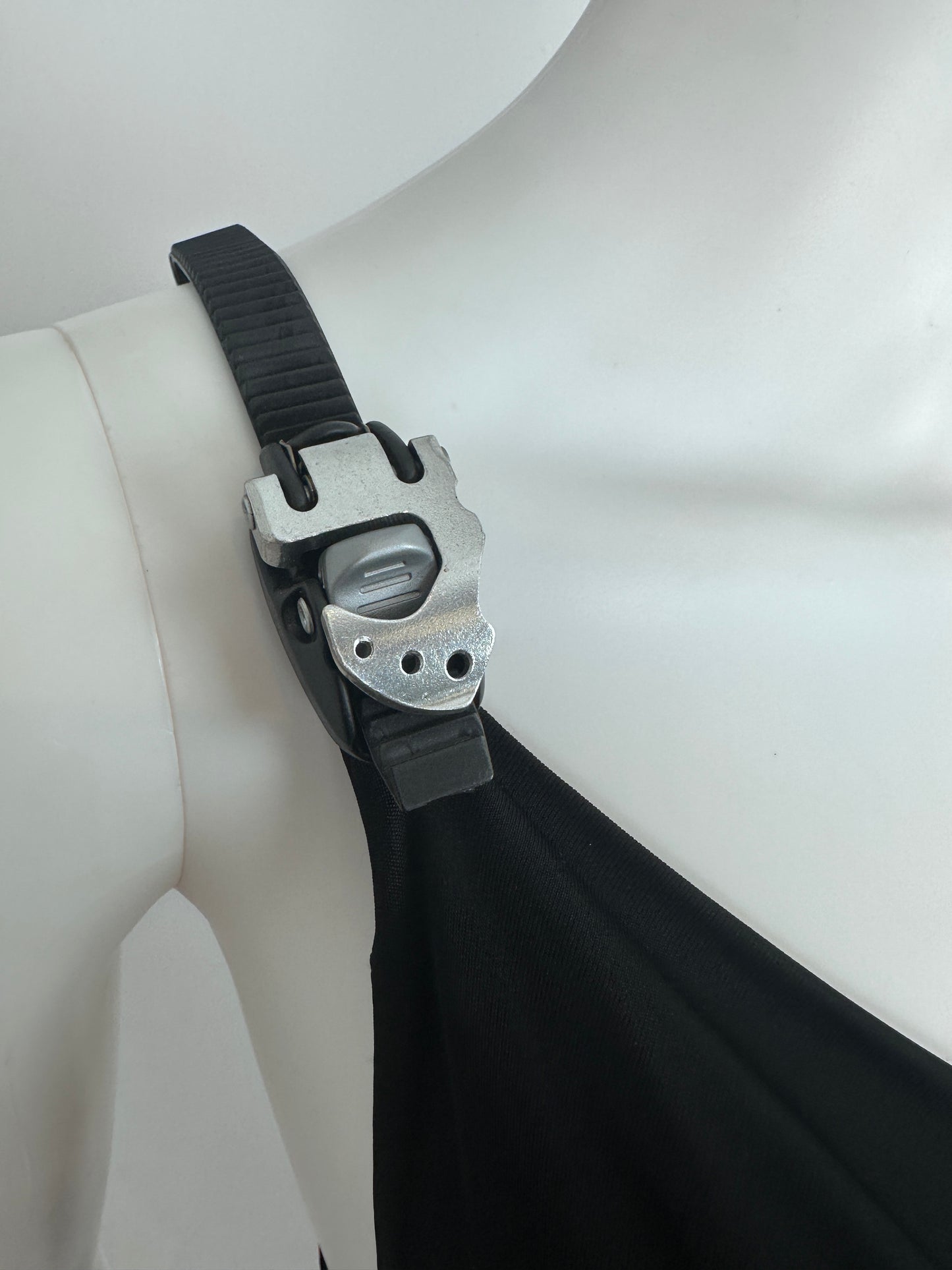 Close-up of a black strap with a silver metal buckle attached to a white mannequin torso.