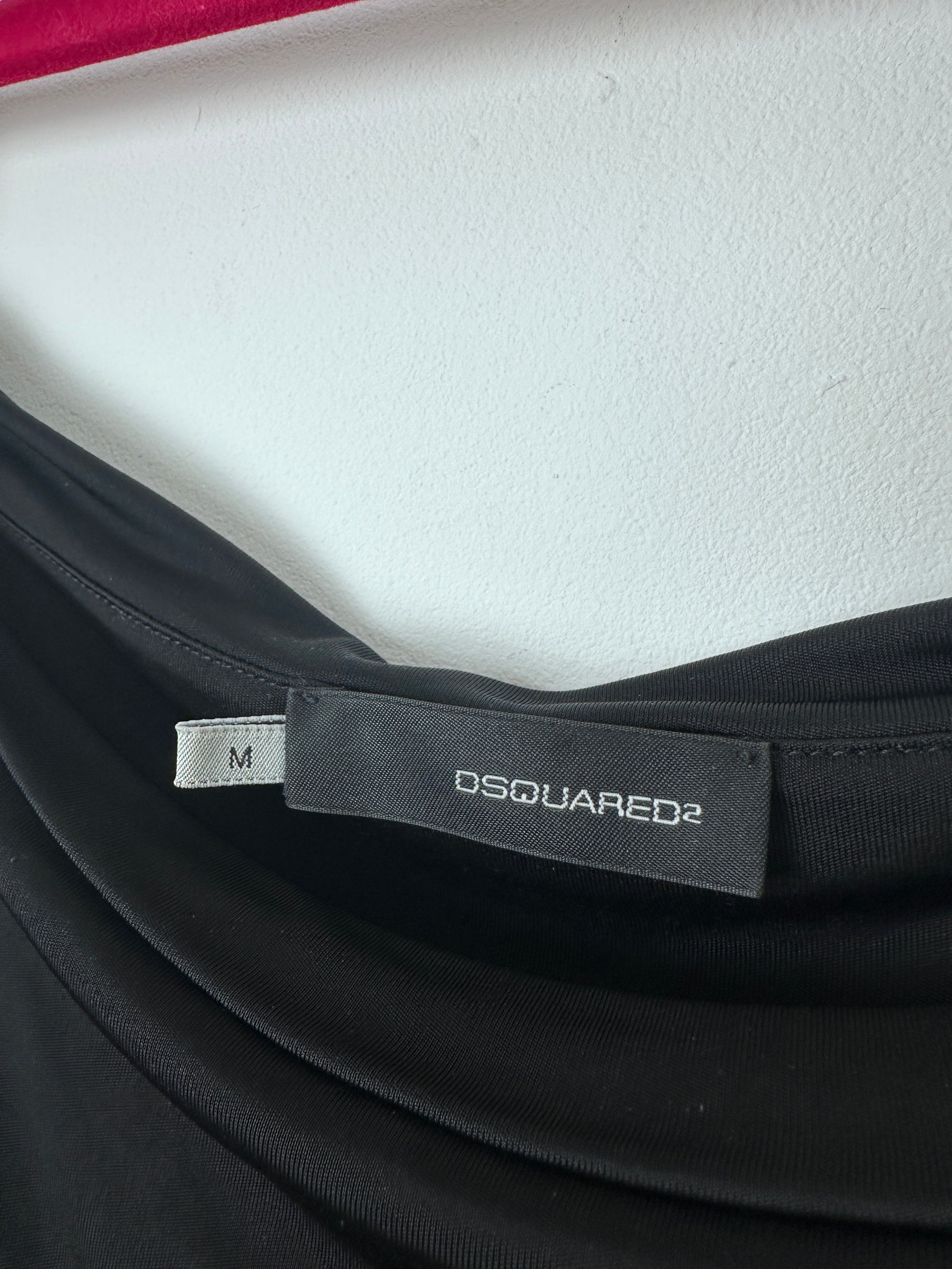 Close-up of a black garment with a visible Dsquared2 brand label and a small size tag marked M, photographed against a white textured background.